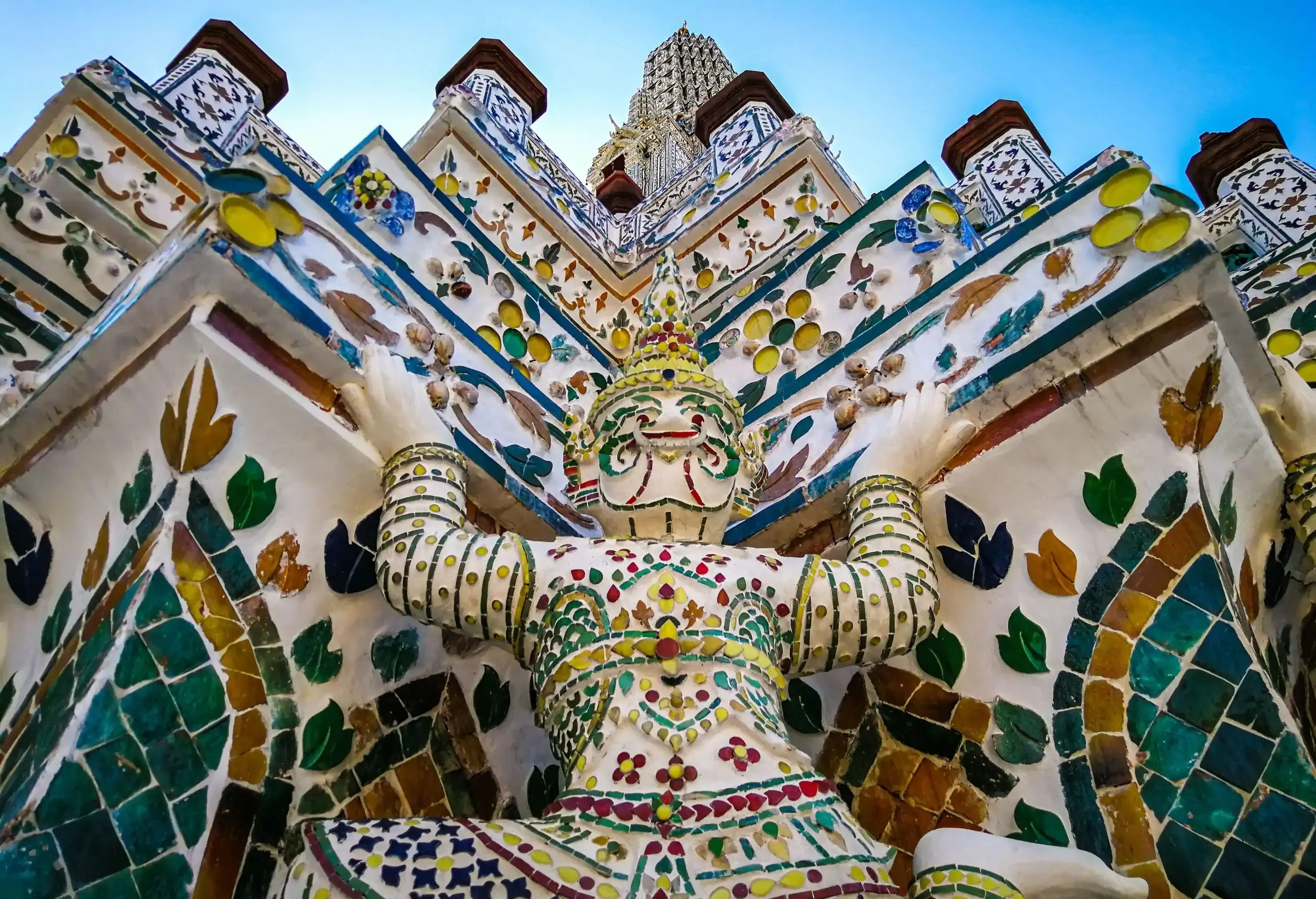 A white statue of a person raising their hand on a temple wall covered in colourful ceramic tiles.
