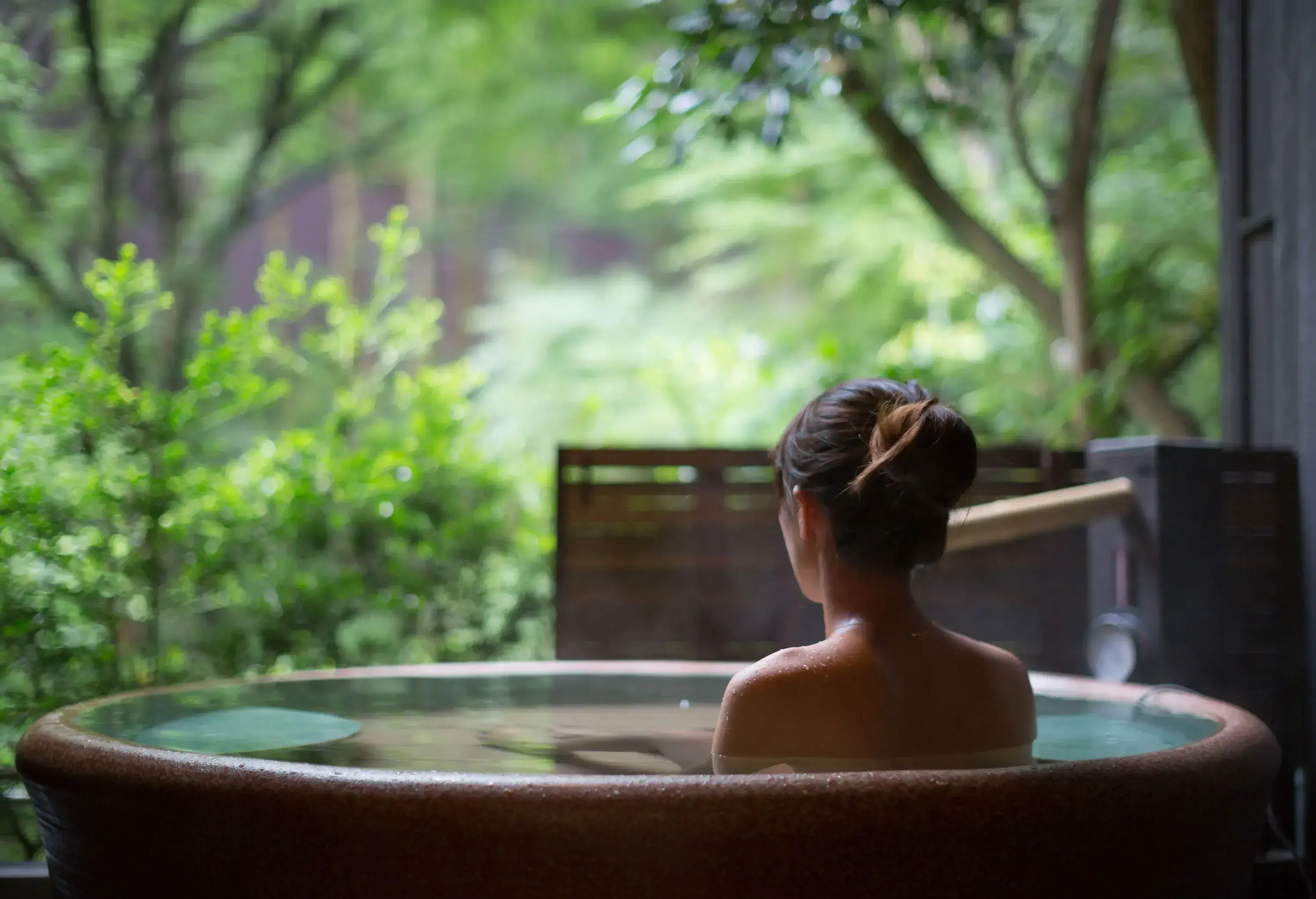 A woman sits in a hot spring bath tub while enjoying the nature's scenery.