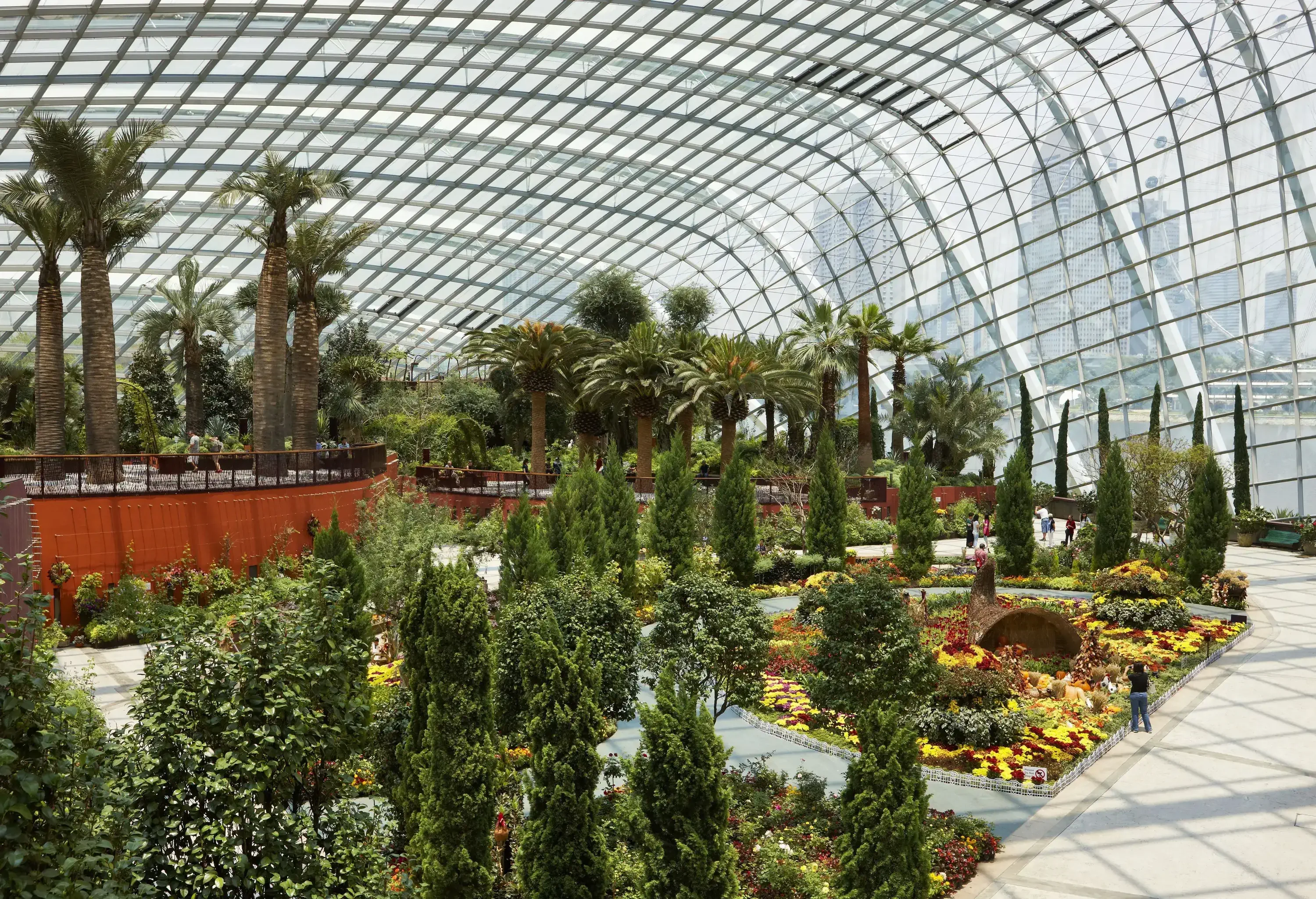 An enormous conservatory filled with towering trees and vibrant flower beds.