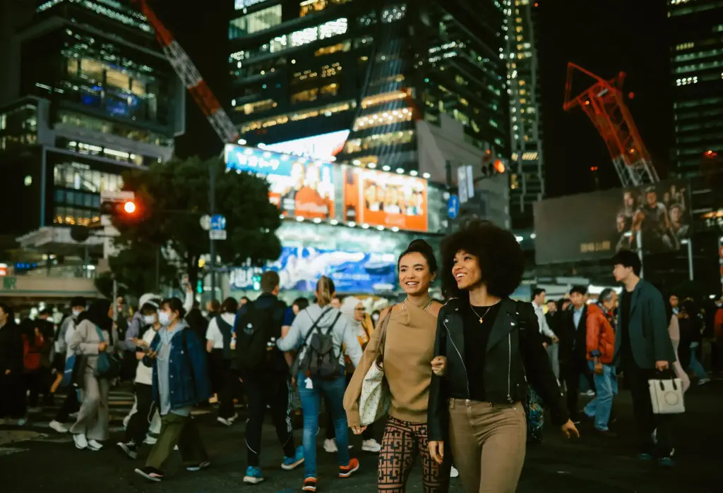 Fashionable young women visiting Tokyo, walking through the bustling streets of Shibuya, soaking in the energy of the city in the evening, lit by the neon lights. Gen Z travel concepts in Tokyo, Japan.