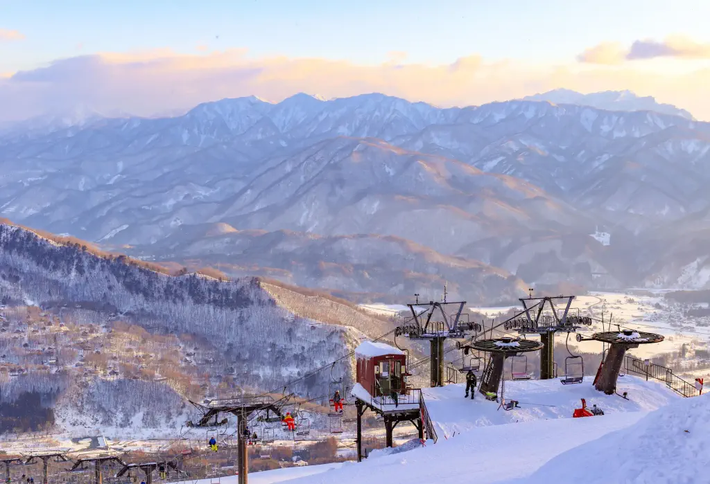 As the chairlift ascends, riders are treated to a stunning view of the snow-covered landscape below, with a majestic mountain range stretching out in the distance.