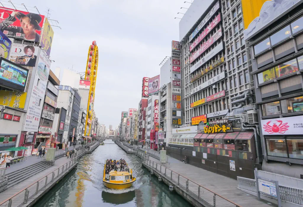 A group of people on a boat tour along Dotonbori canal, passing by well-known shops and entertaining spots.