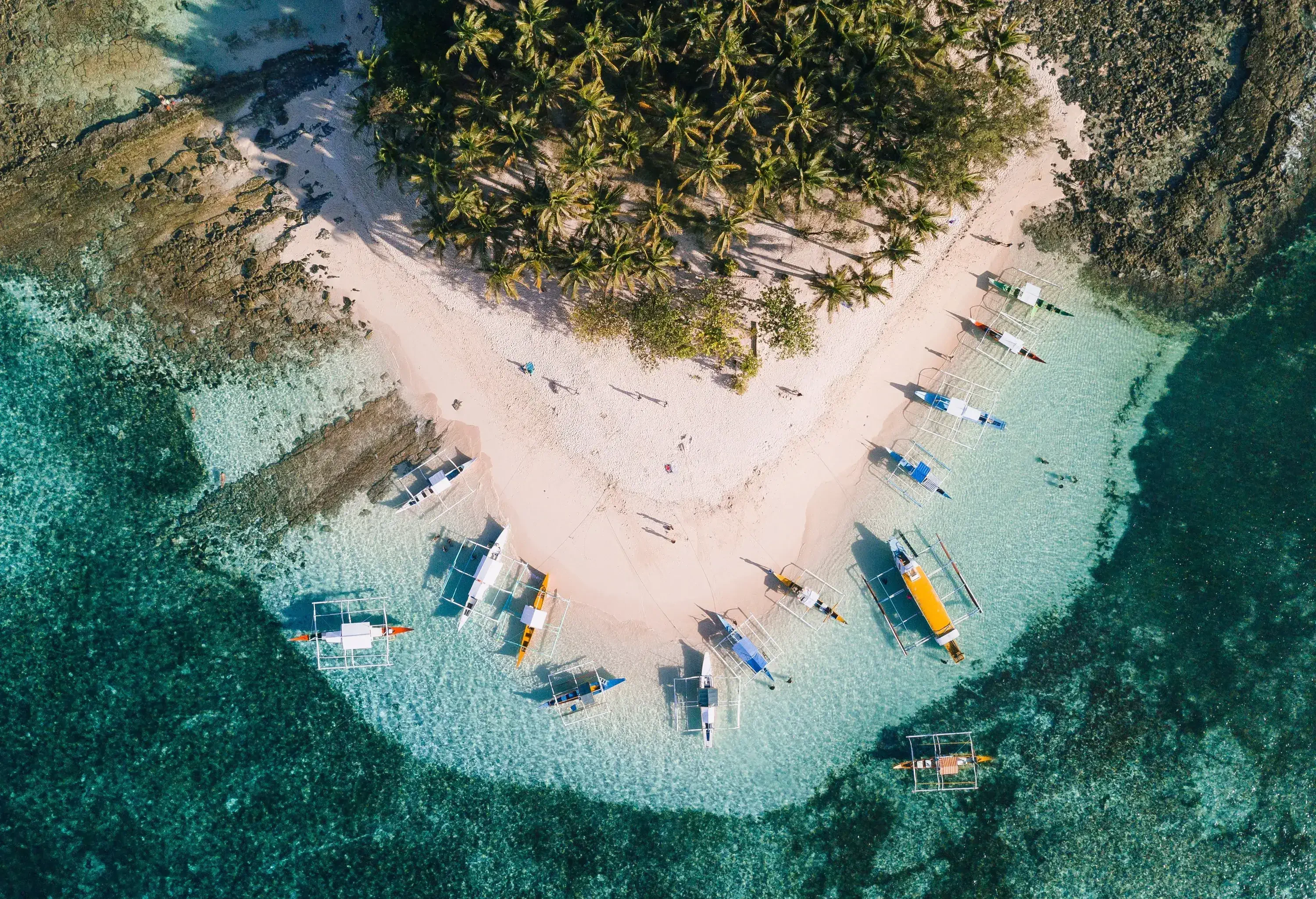 Pristine white beach along a grove of palm trees with tour boats floating on crystal-clear waters.