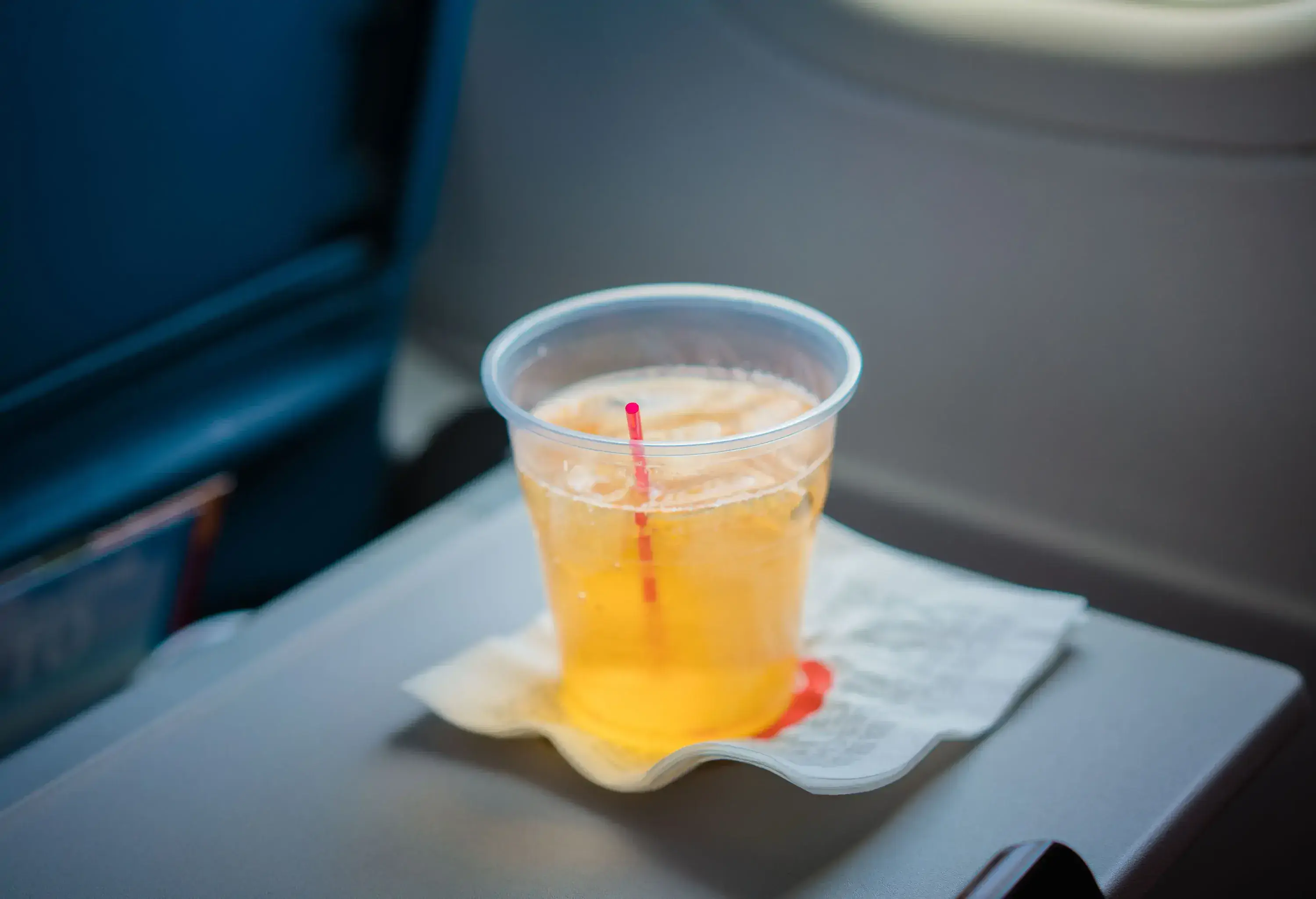 A plastic cup of yellow drink with ice on a tray table.