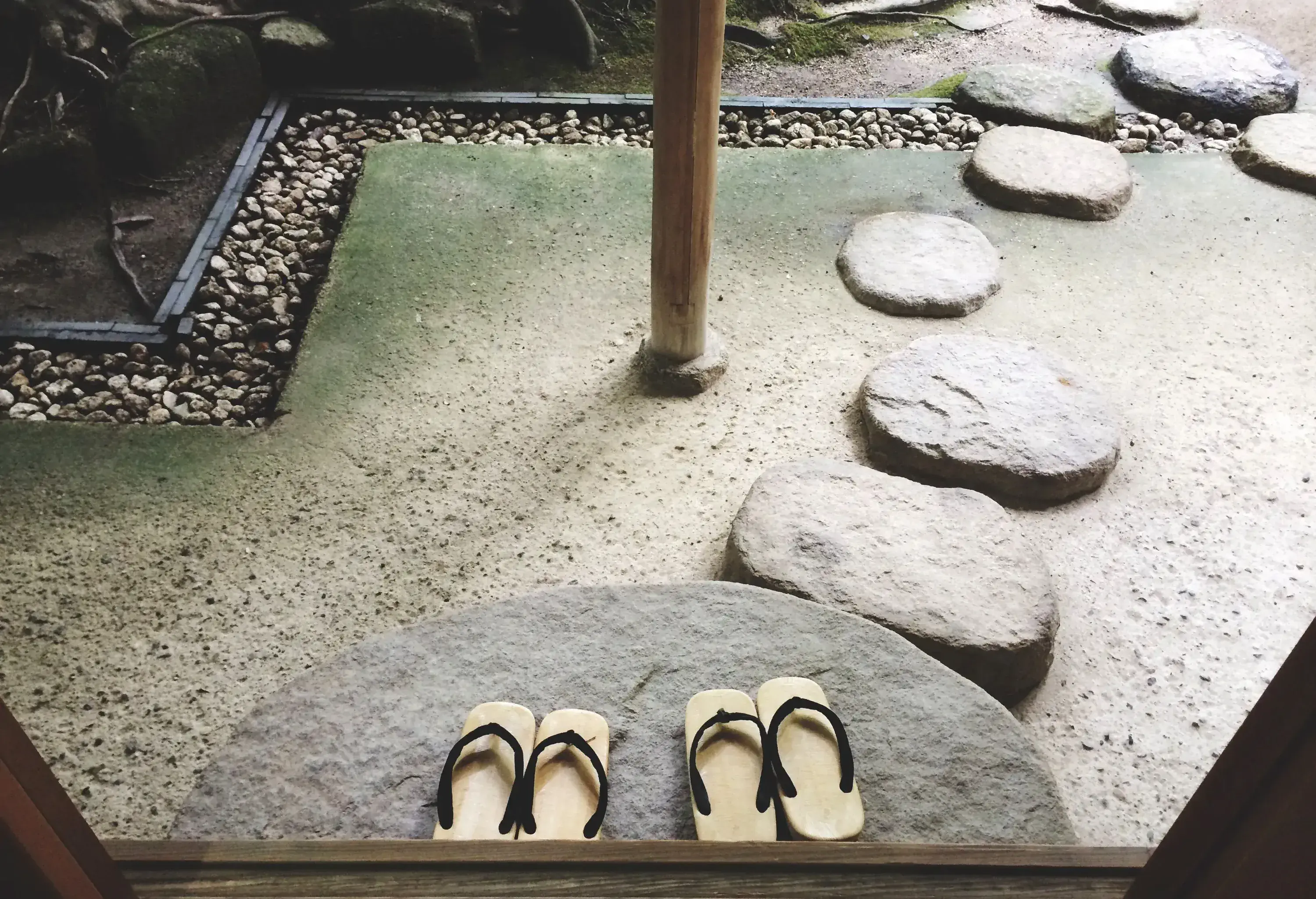 A room's entrance with two pairs of slippers placed on stone pavers.