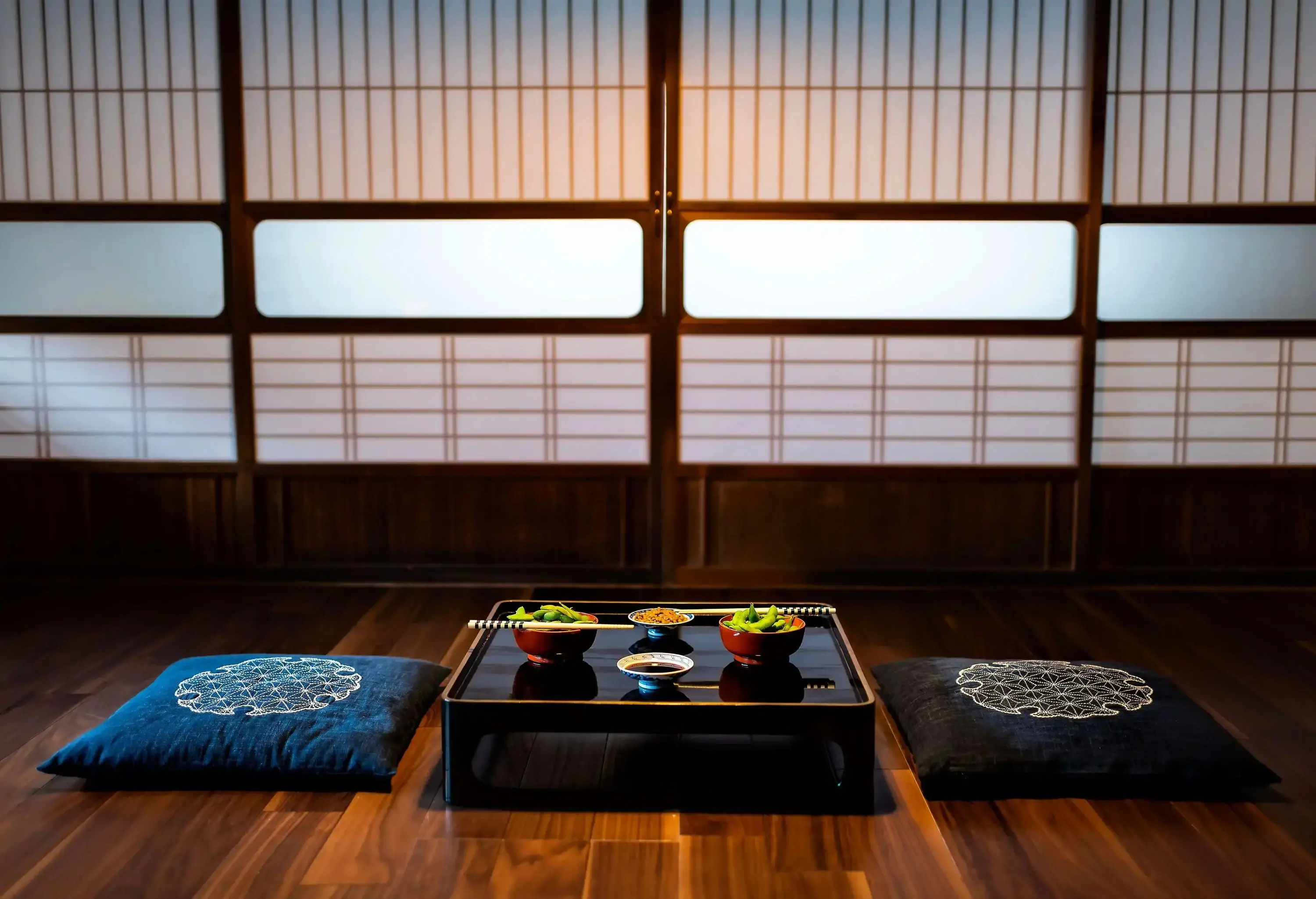 Two meal bowls served on a black low lacquered table with cushions on the wooden floor.