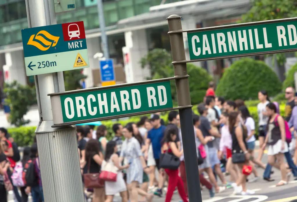 The Orchard Road and Cairnhill Road signage, with a throng of pedestrians crossing the street in the backdrop.