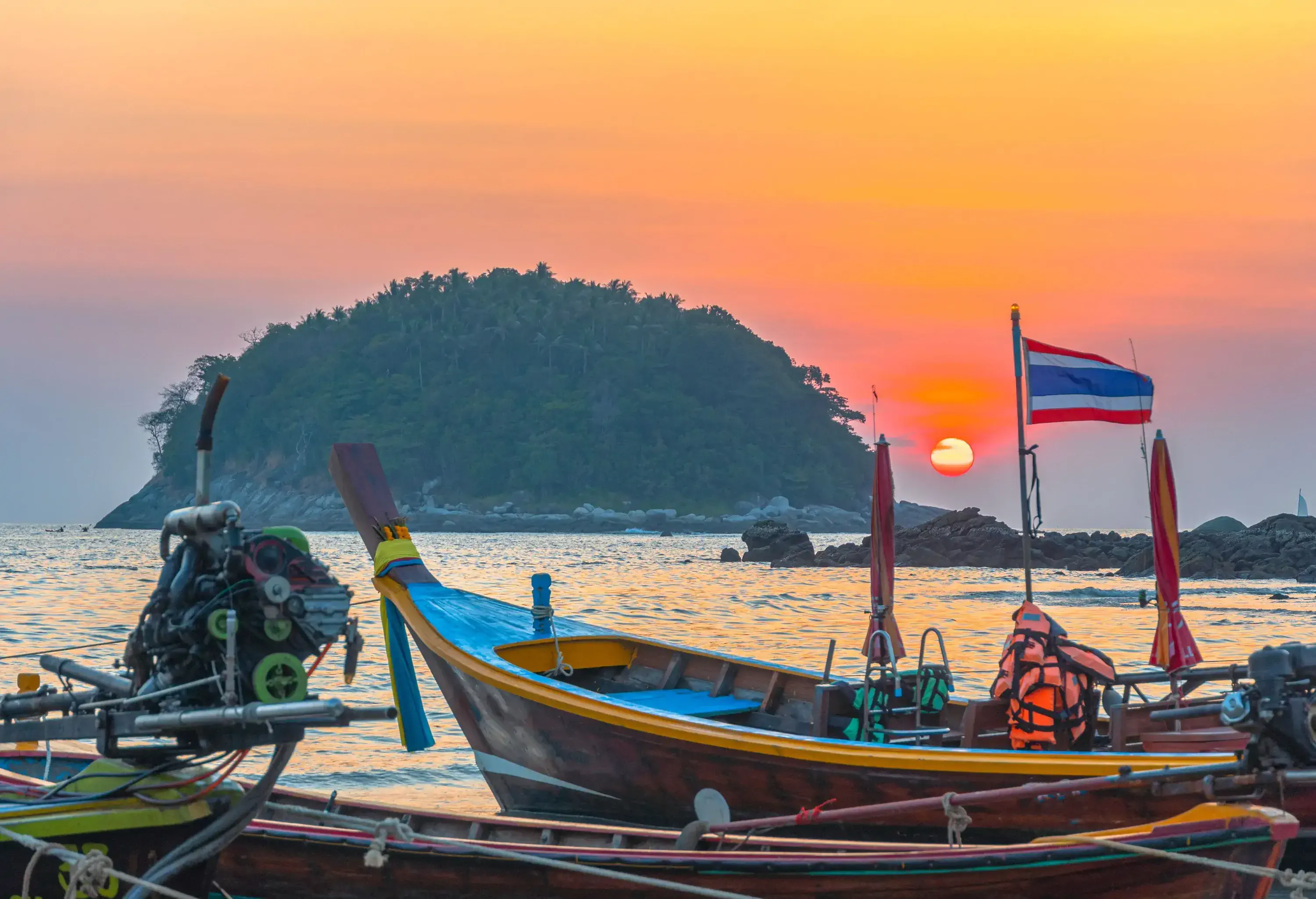 Wooden fishing boats on the shore overlooking a lush island in the middle of the sea against the scenic sunset sky.