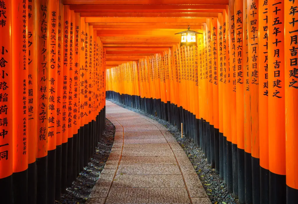 A pathway lined with orange pillars with Japanese inscriptions.