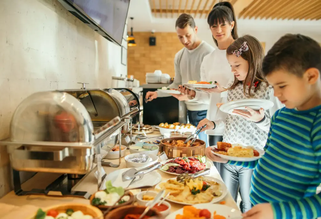 Family taking food in self service restaurant in hotel. A lot of domestic colorful food is served. Family with two children.