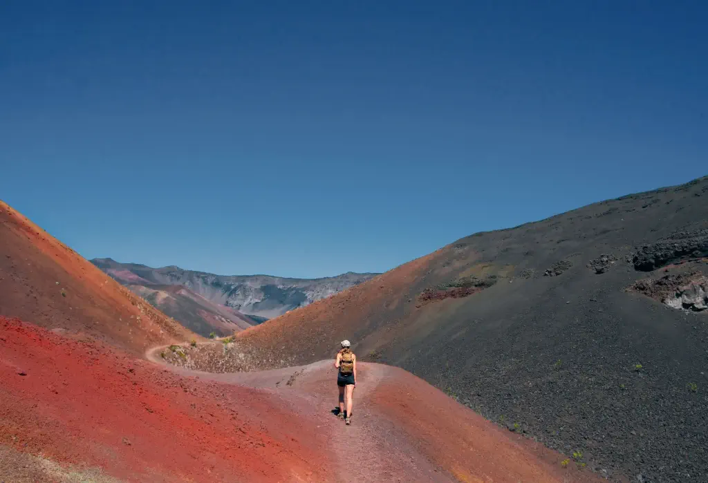 A girl embarks on an adventure, hiking through the mesmerizingly colourful sand slopes of Haleakalā National Park.