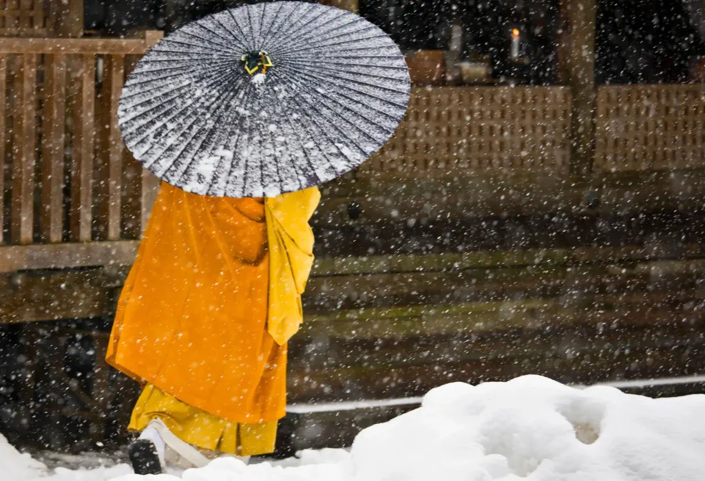 A Buddhist monk walks in the heavy snowfall with his black umbrella.