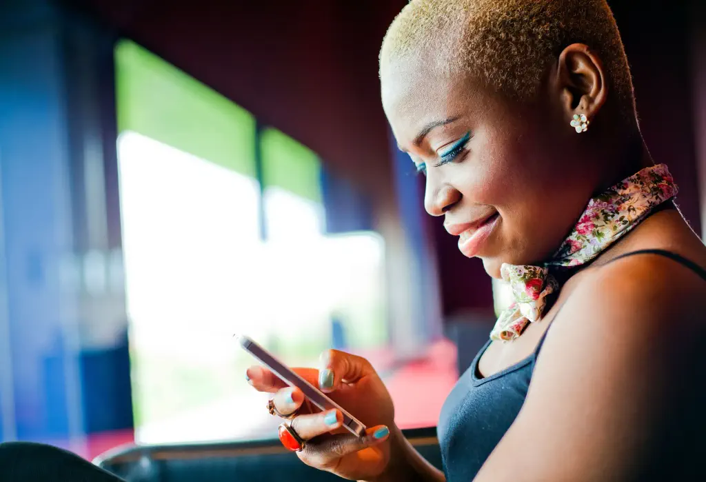 A woman with a shaved haircut smiles as she looks at her phone.