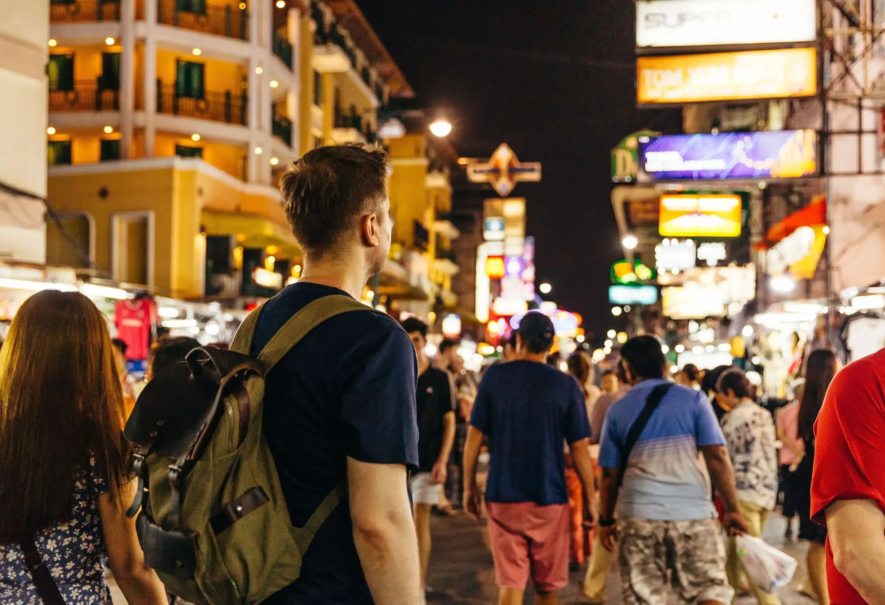 A crowd of people on a busy road lined with brightly lit buildings.