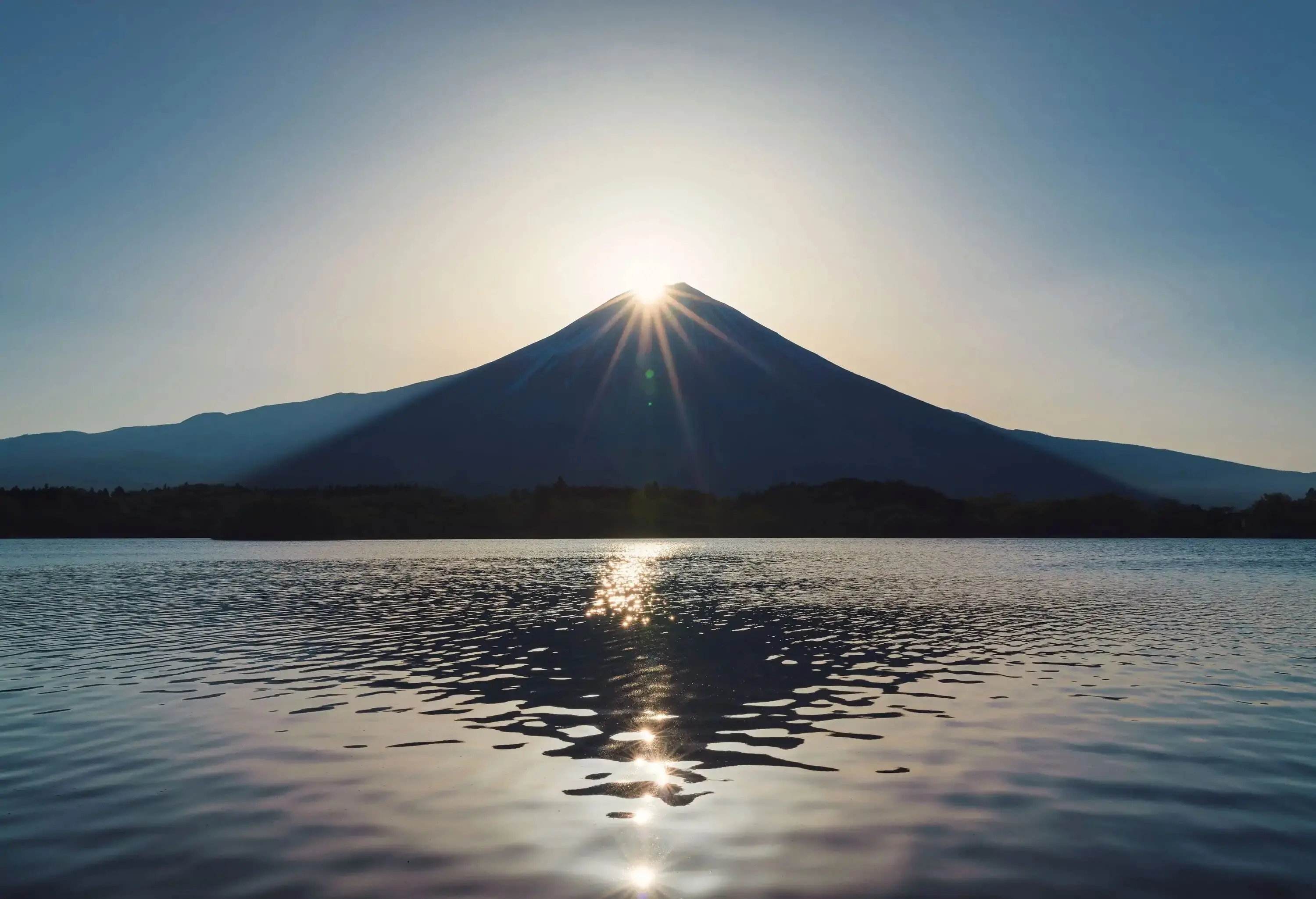 A shimmering lake and the bright sun that is rising over the mouth of Mount Fuji.