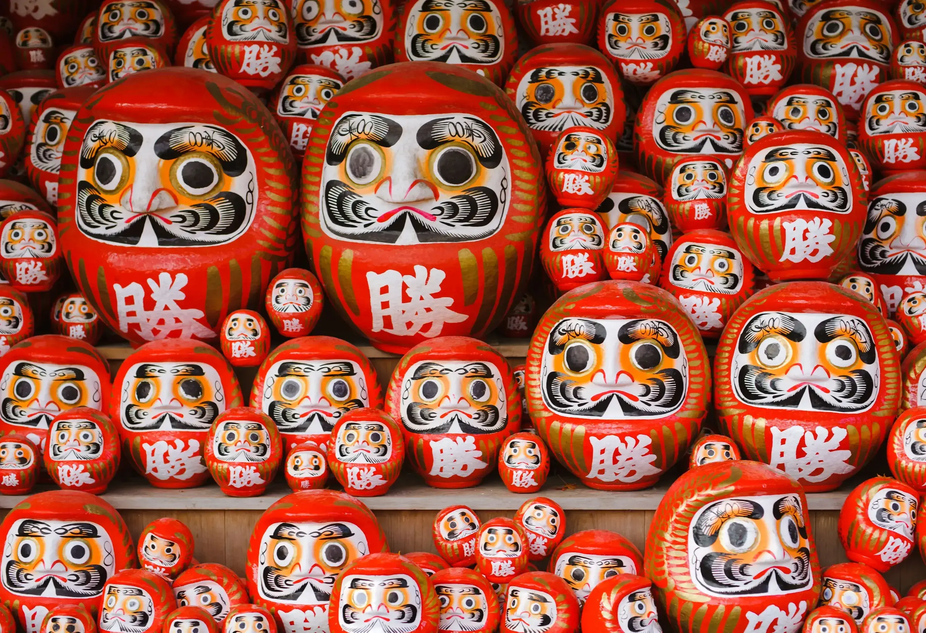 A display of orange and round Japanese dolls with hand-painted faces in different sizes.