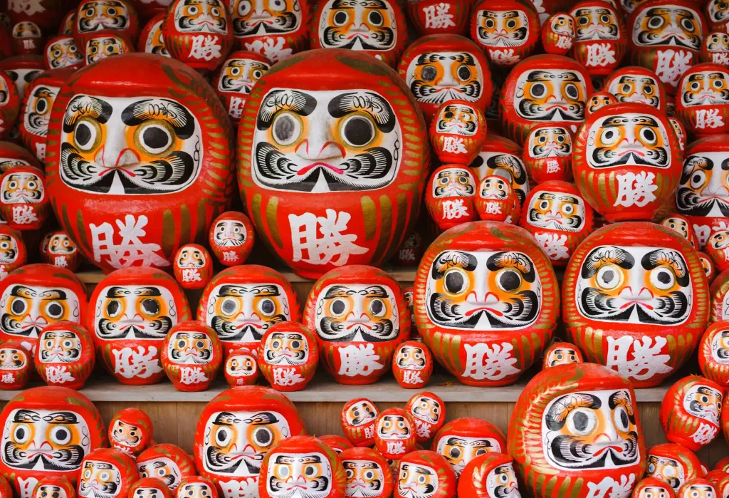 A display of orange and round Japanese dolls with hand-painted faces in different sizes.