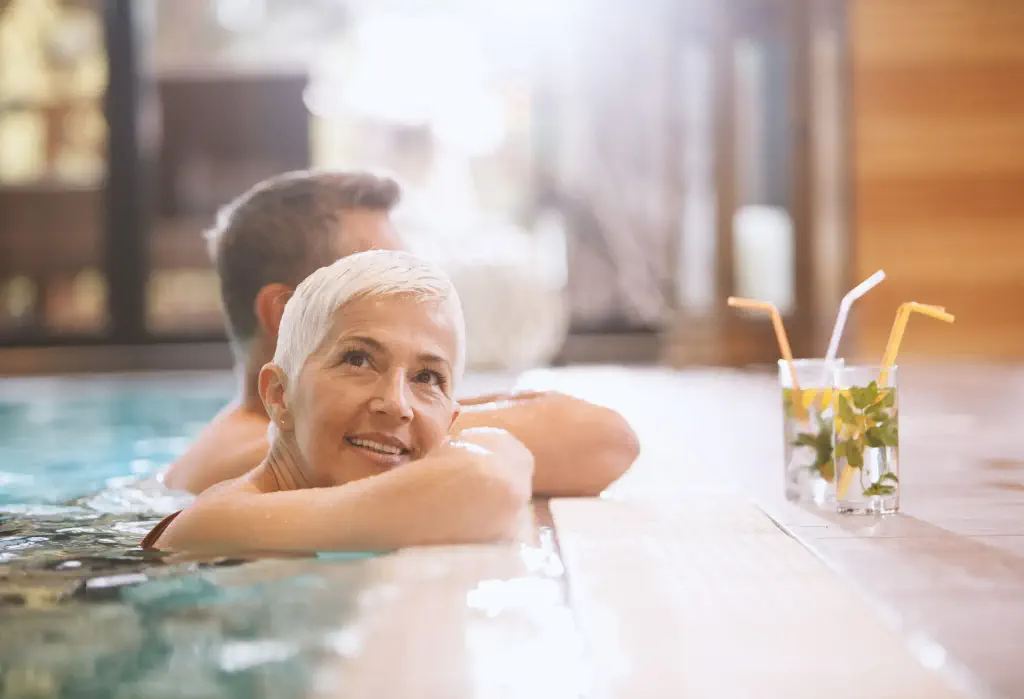 A couple having a glass of drinks while soaking in an indoor swimming pool spa.