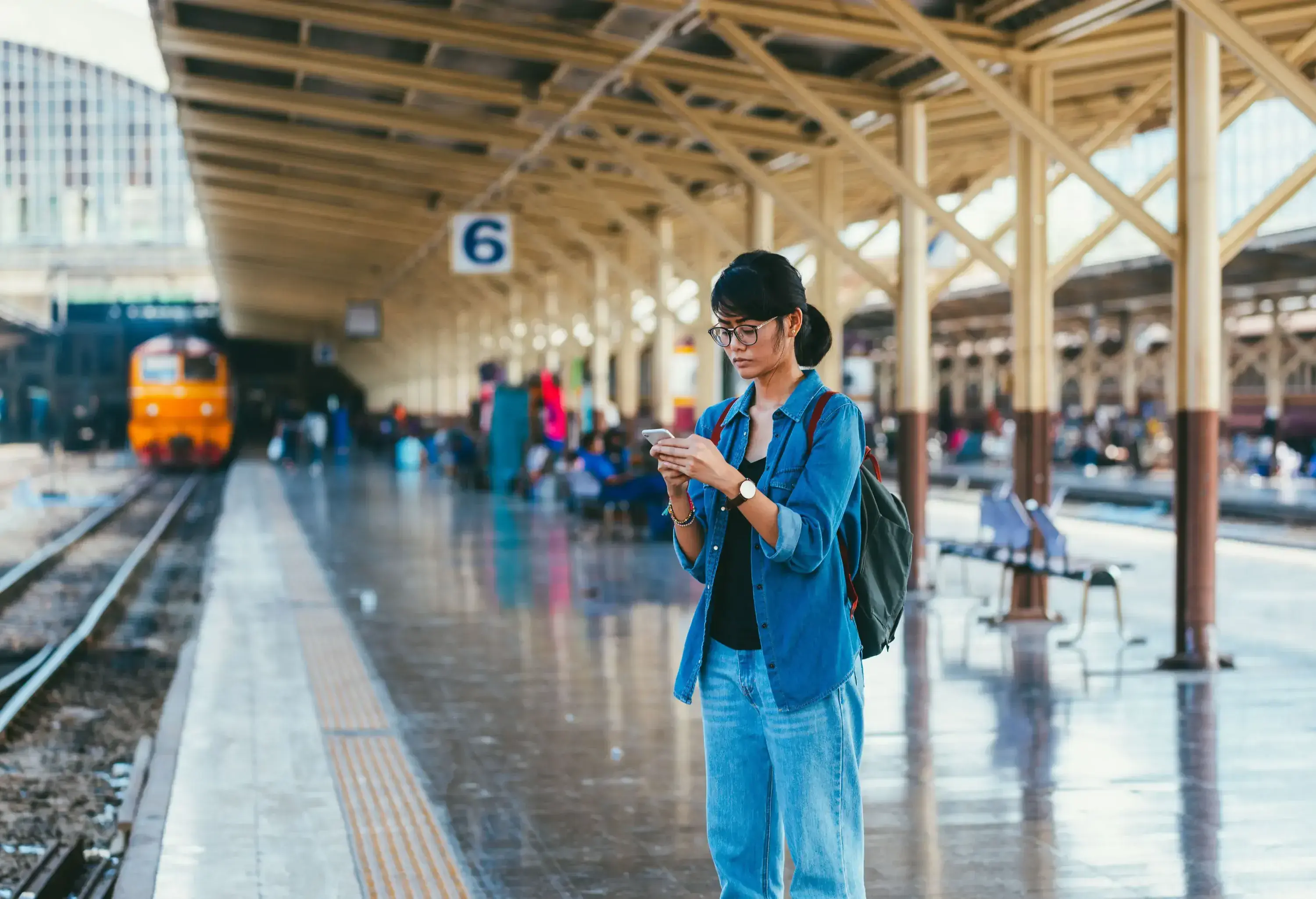 A woman is standing at a train station, looking at her mobile phone.