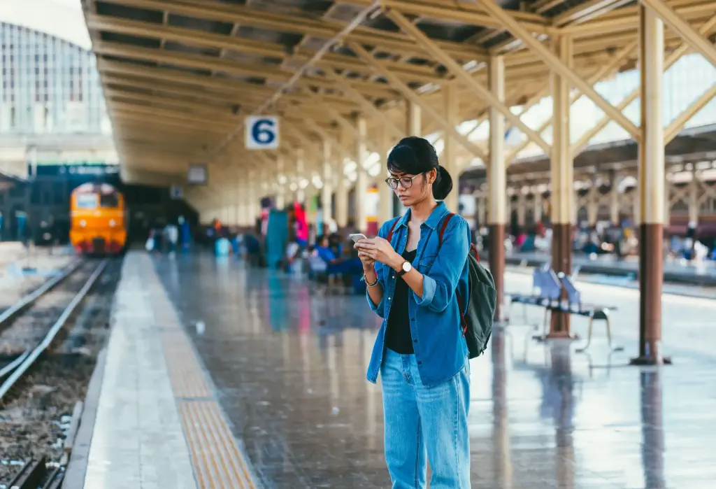 A woman is standing at a train station, looking at her mobile phone.