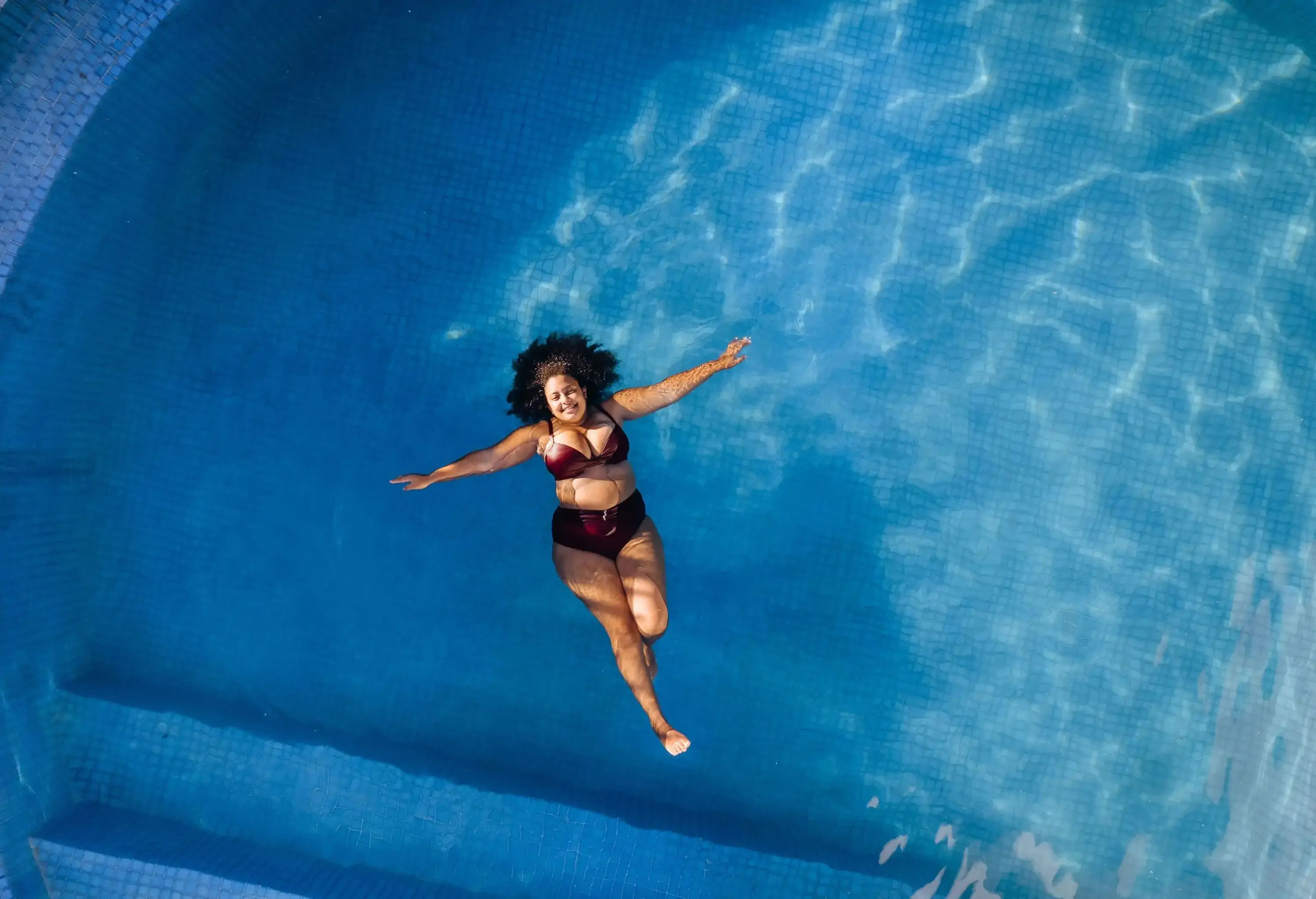 A woman in a bikini relaxes in a swimming pool, floating peacefully in the cool and refreshing water.