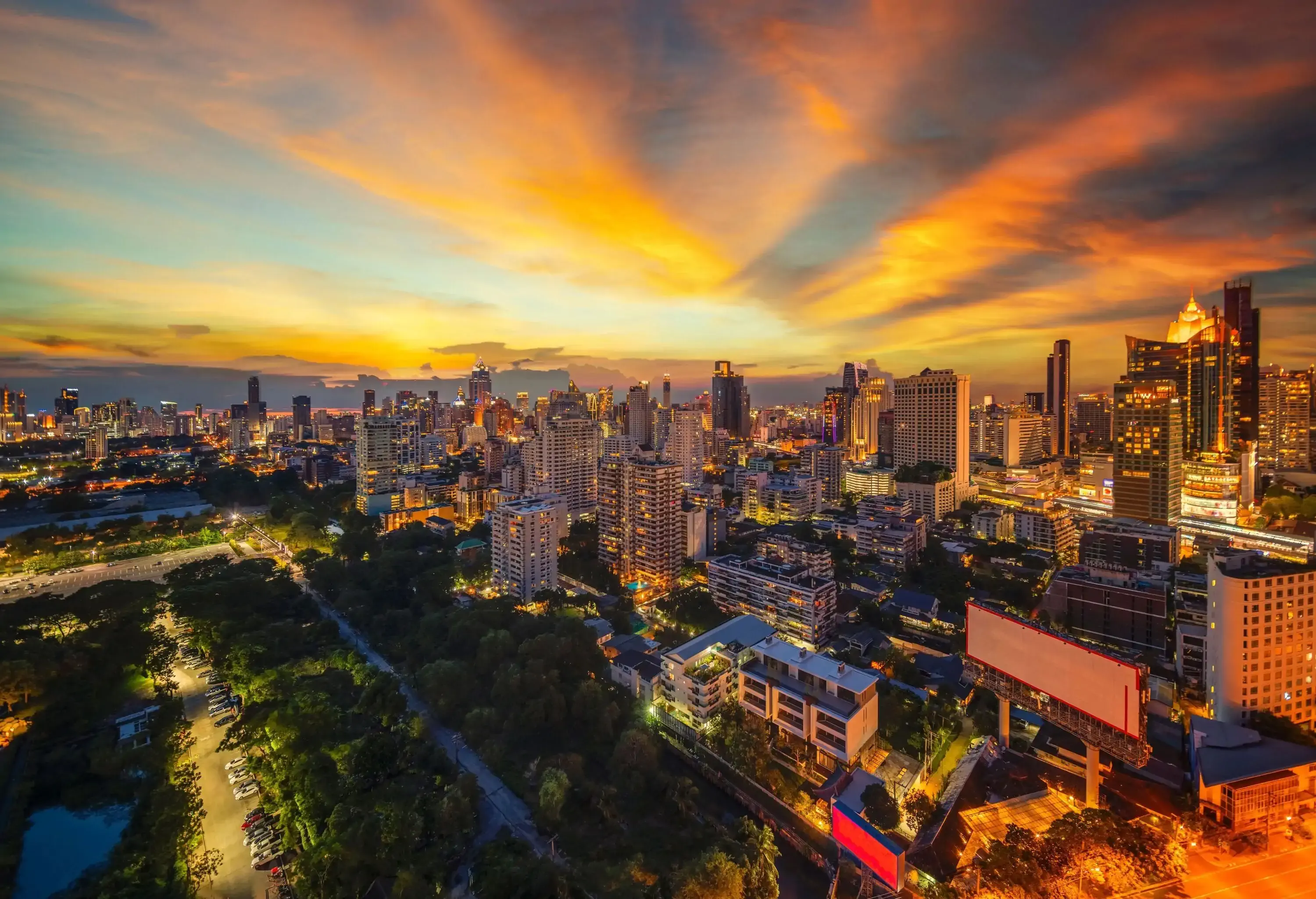 An urban landscape with high-rise buildings and trees under the glowing sunset sky.