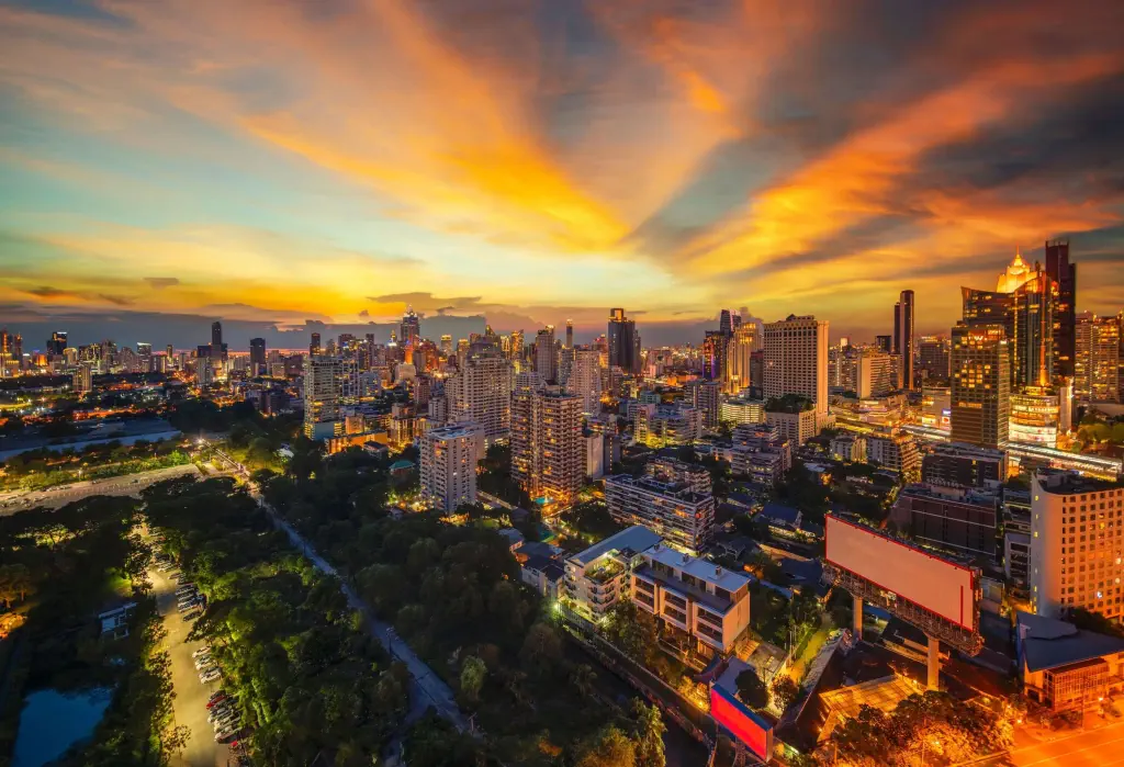 An urban landscape with high-rise buildings and trees under the glowing sunset sky.