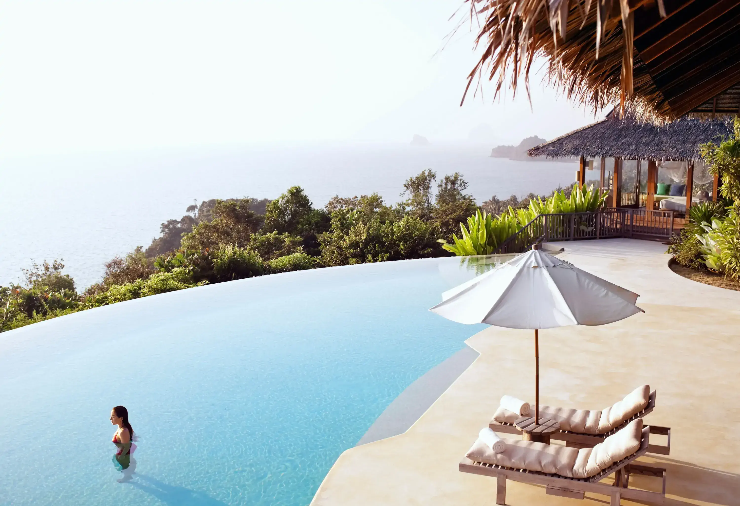 A woman stands in an inviting infinity pool, gazing out over the breathtaking surroundings and tranquil sea.