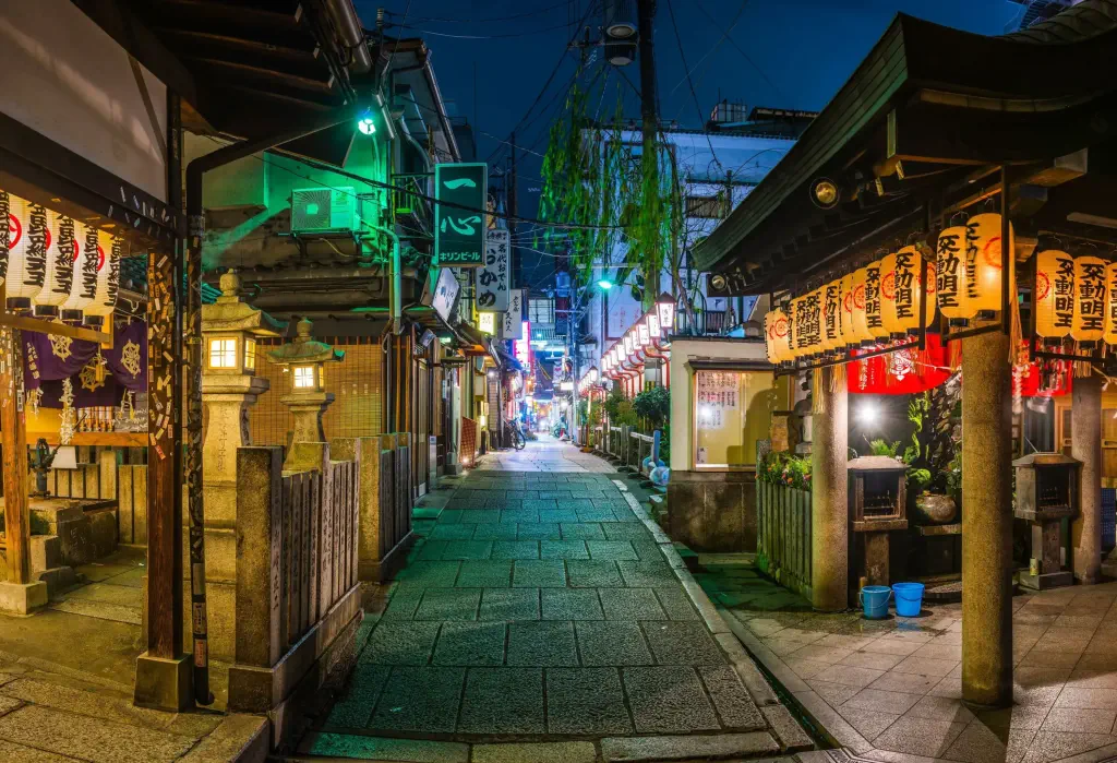 Warm lamplight delicately bathes a serene, paved alleyway lined with quaint buildings.