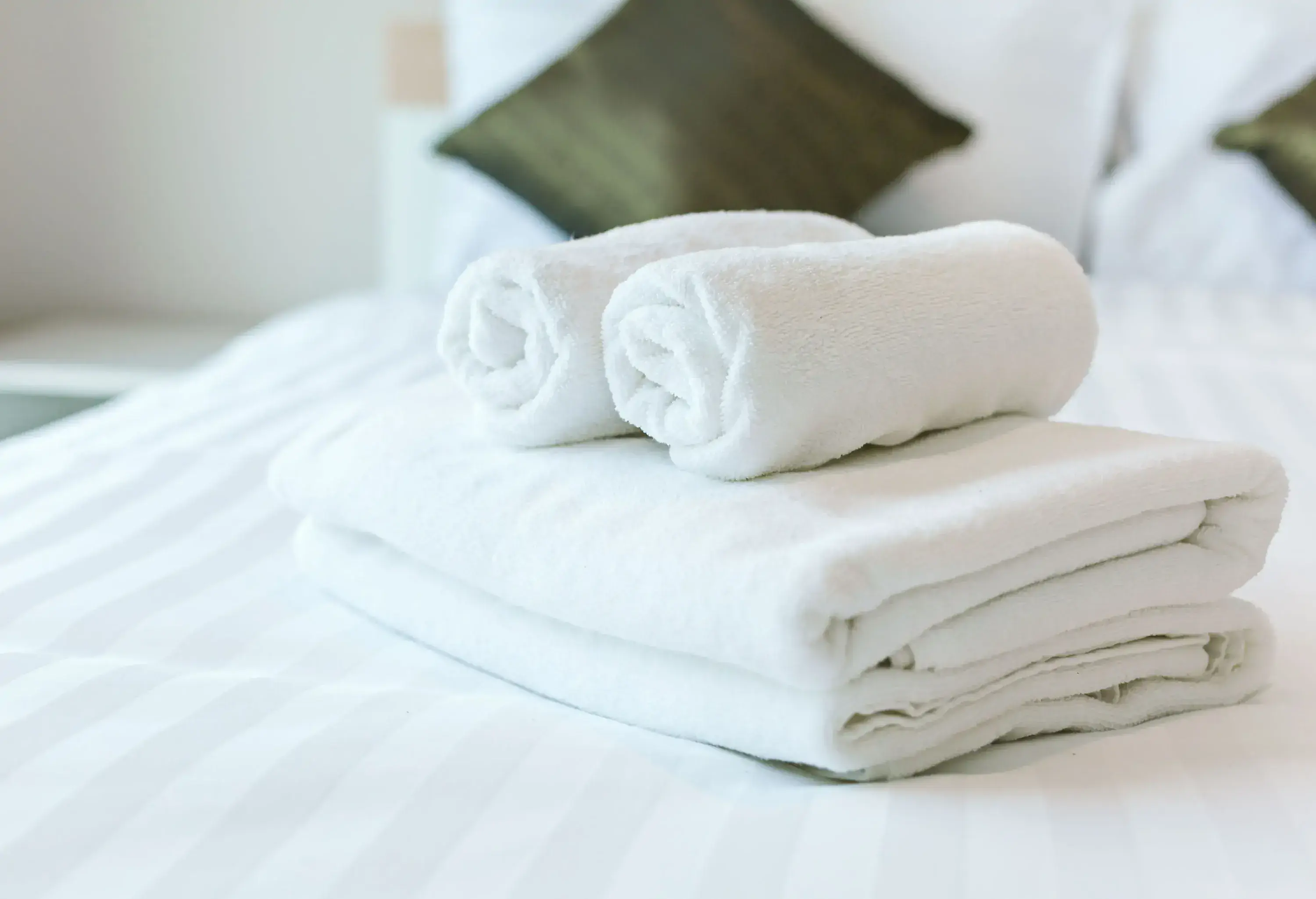 A bed with a stack of freshly folded and rolled white towels.