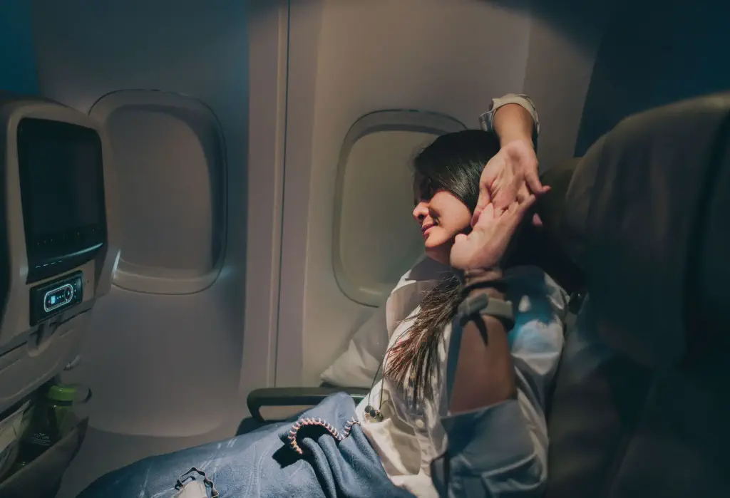 A person stretches their arms overhead in a dimly lit airplane seat.