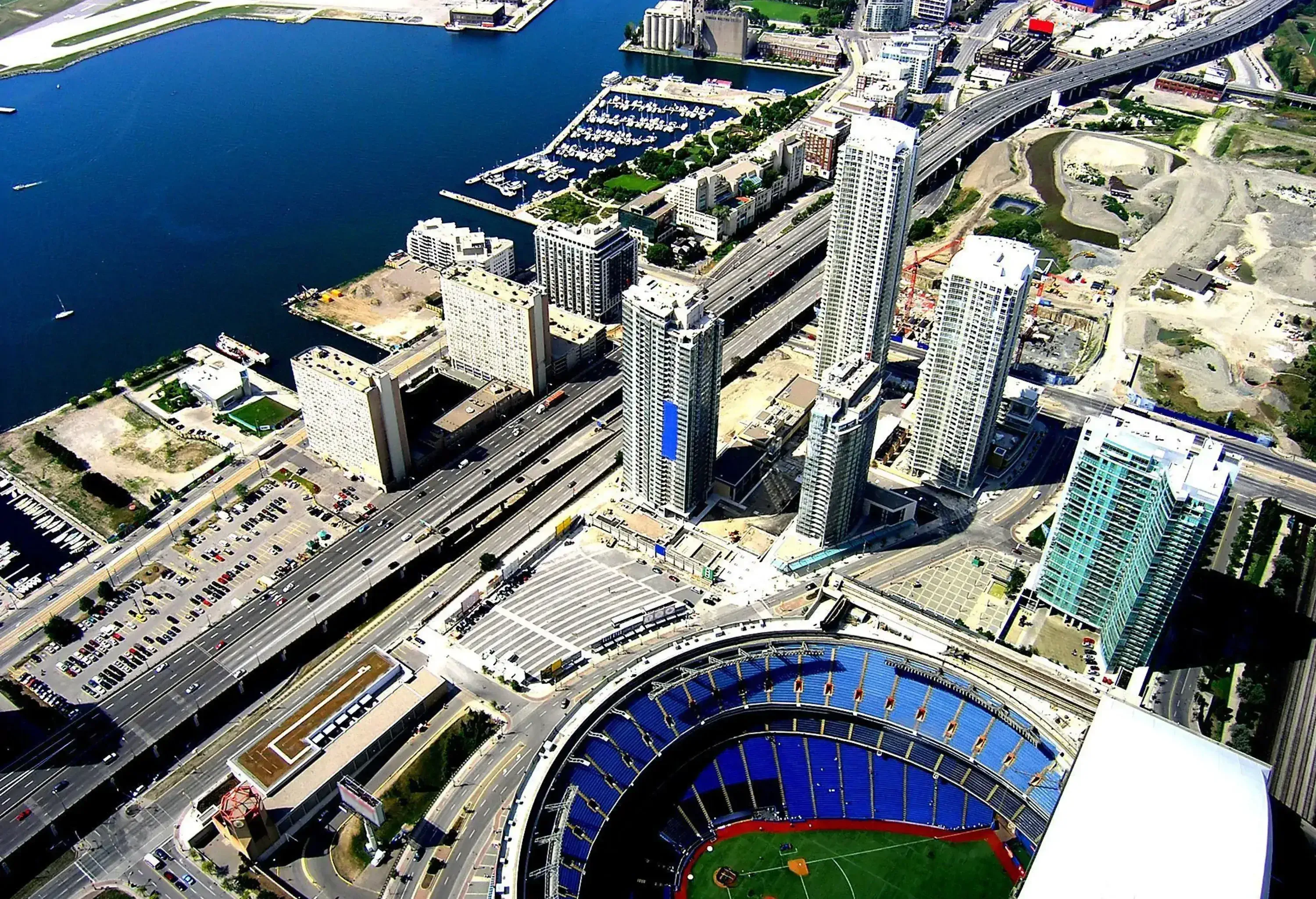 A highway runs through a lakeside city bordered by skyscrapers and a massive stadium.