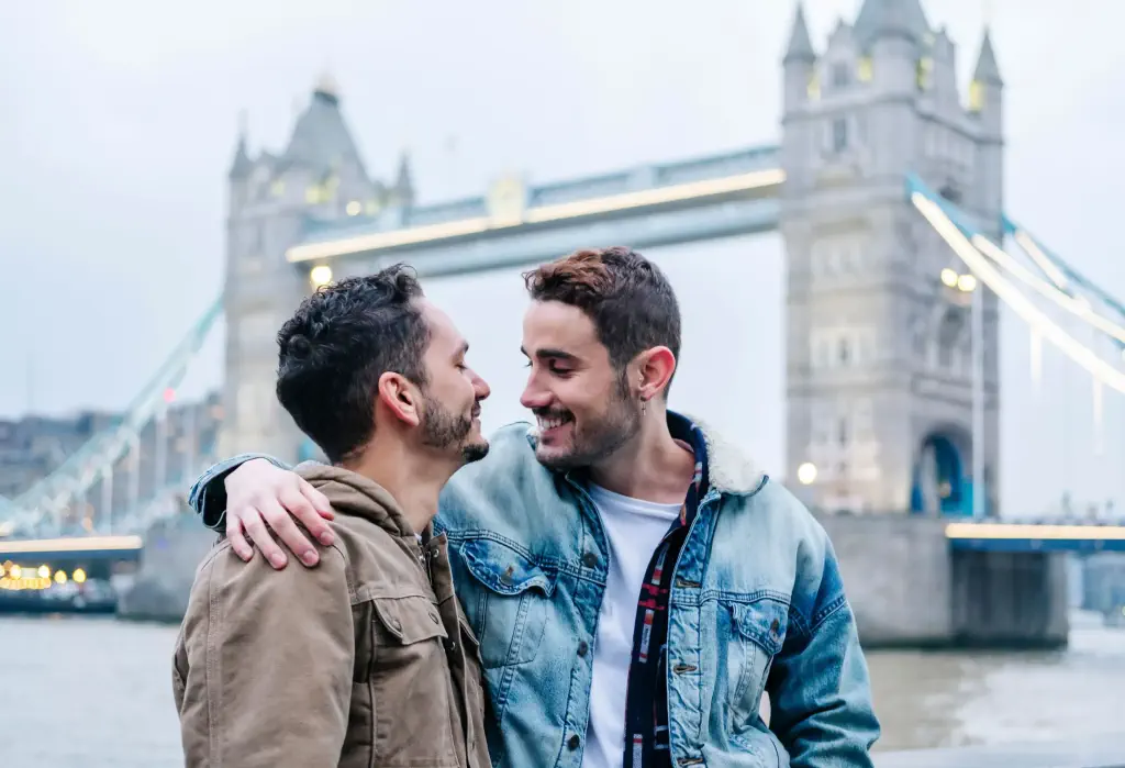Two male friends side-hugging against the London Tower bridge in the background.