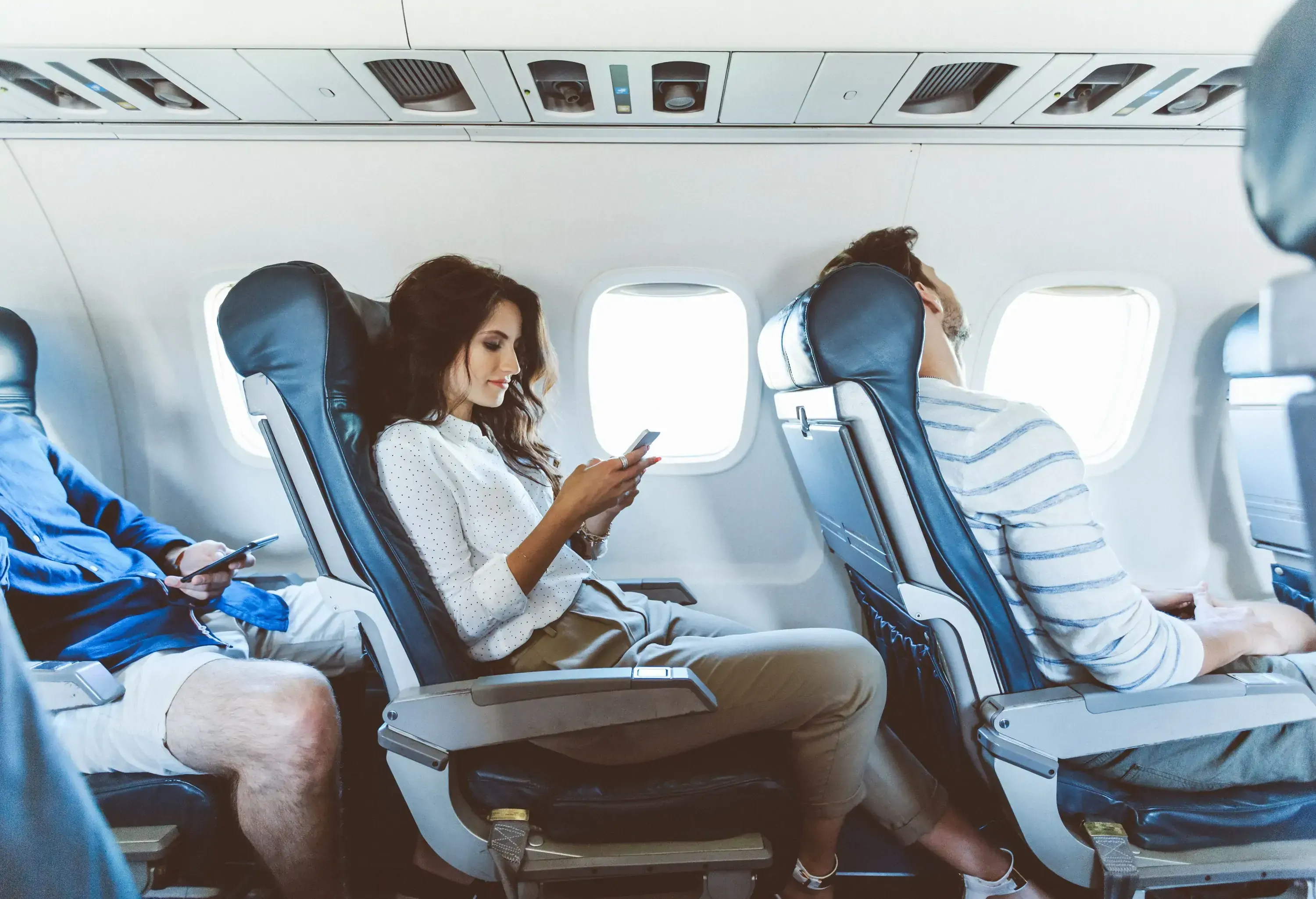 Young woman sitting inside an airplane and using smart phone. Female passenger using phone during flight.