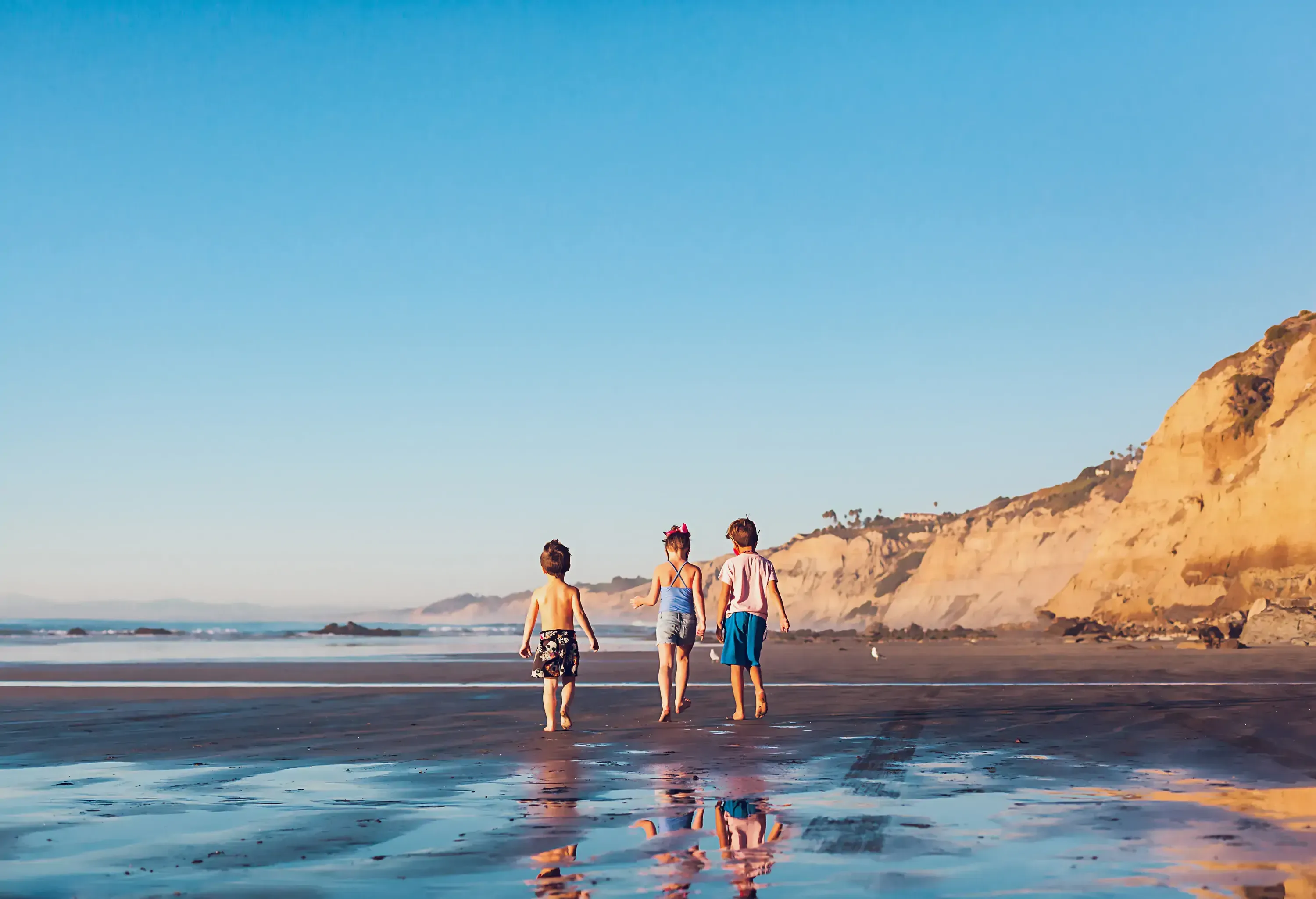 Three little kids walking on a beach