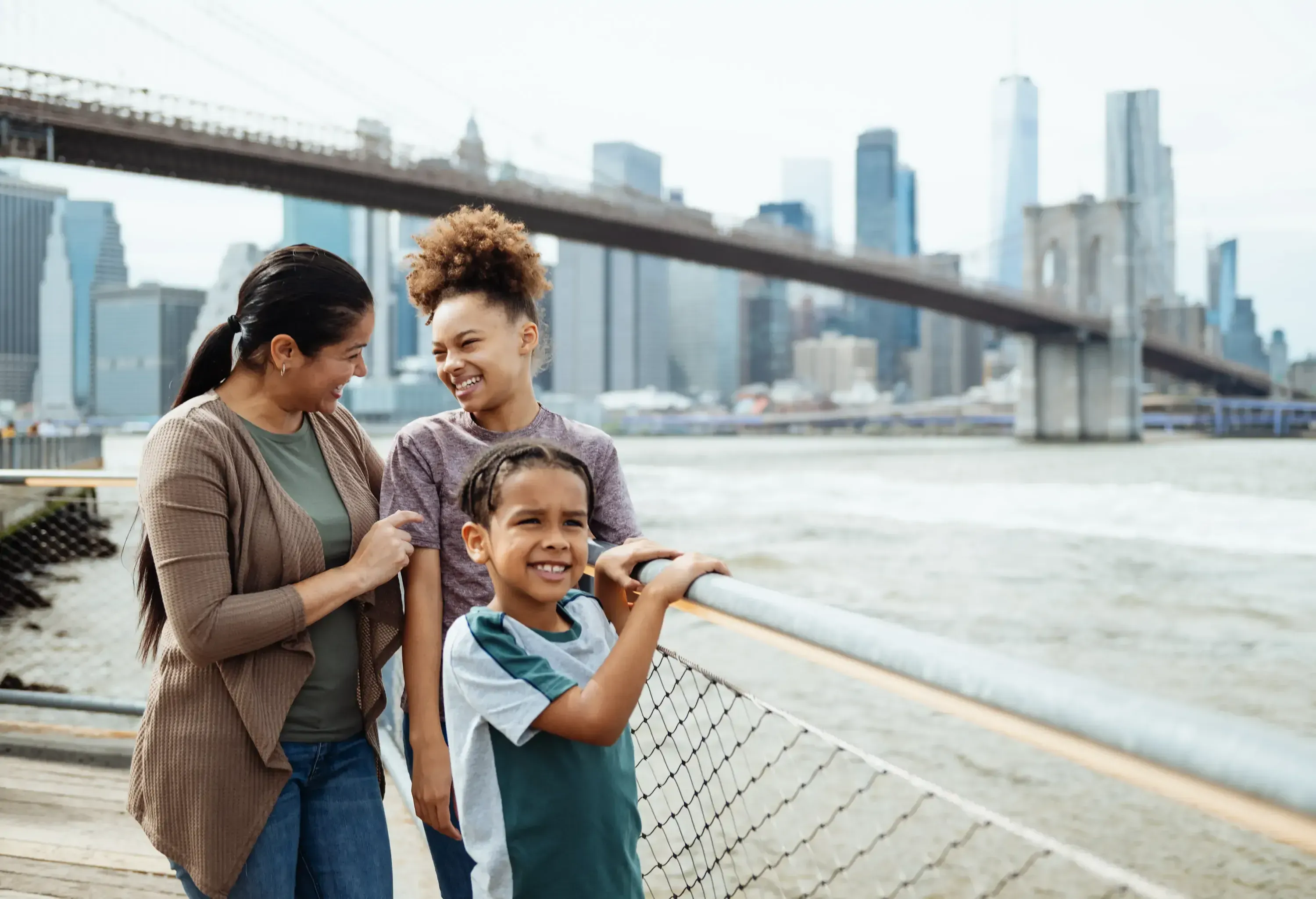 Young family walking by a city river with bridge in the background