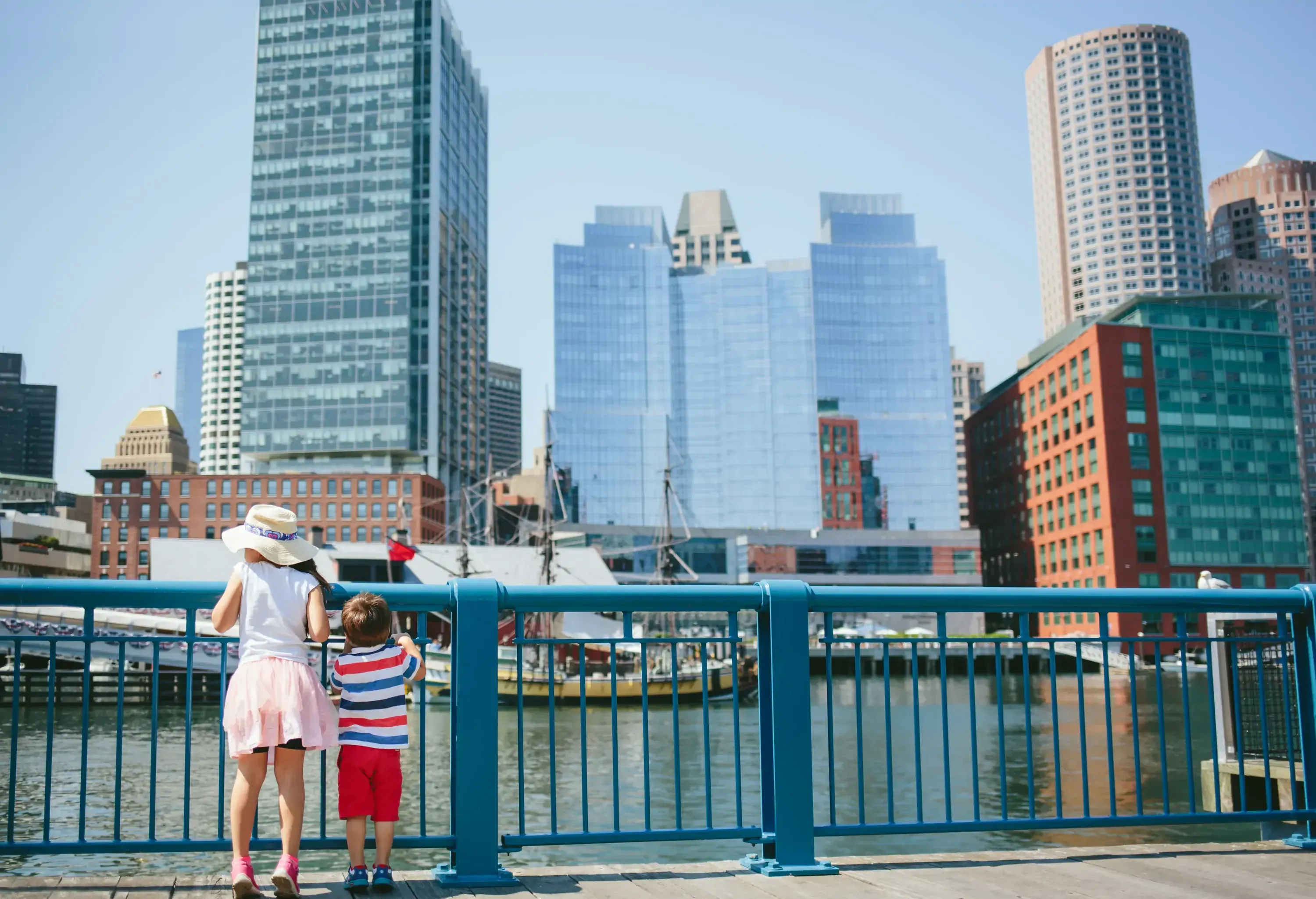 Two children brother and sister overlooking the skyline of a city by the water and clutching a railing
