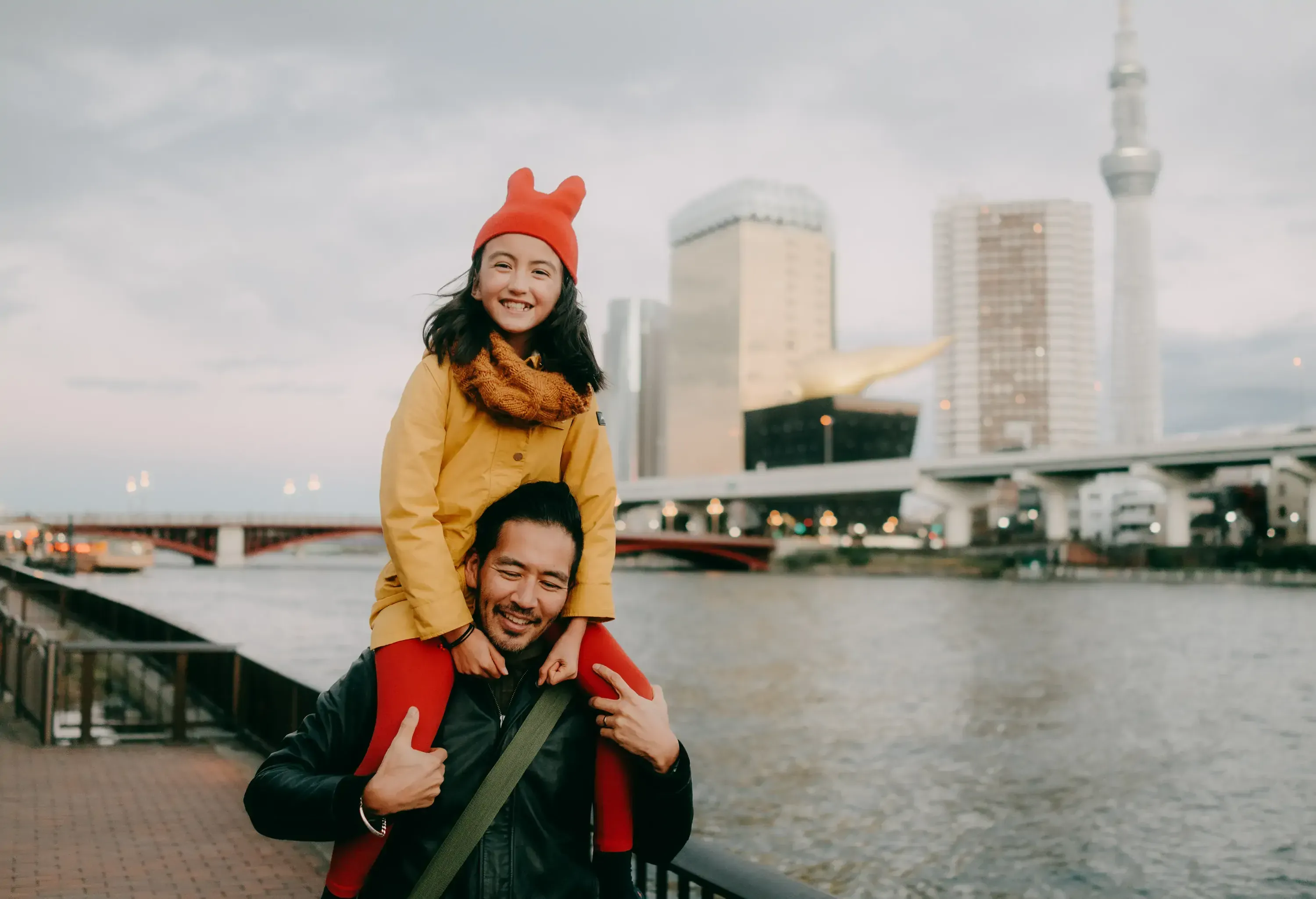 Father giving daughter shoulder ride along urban river in winter