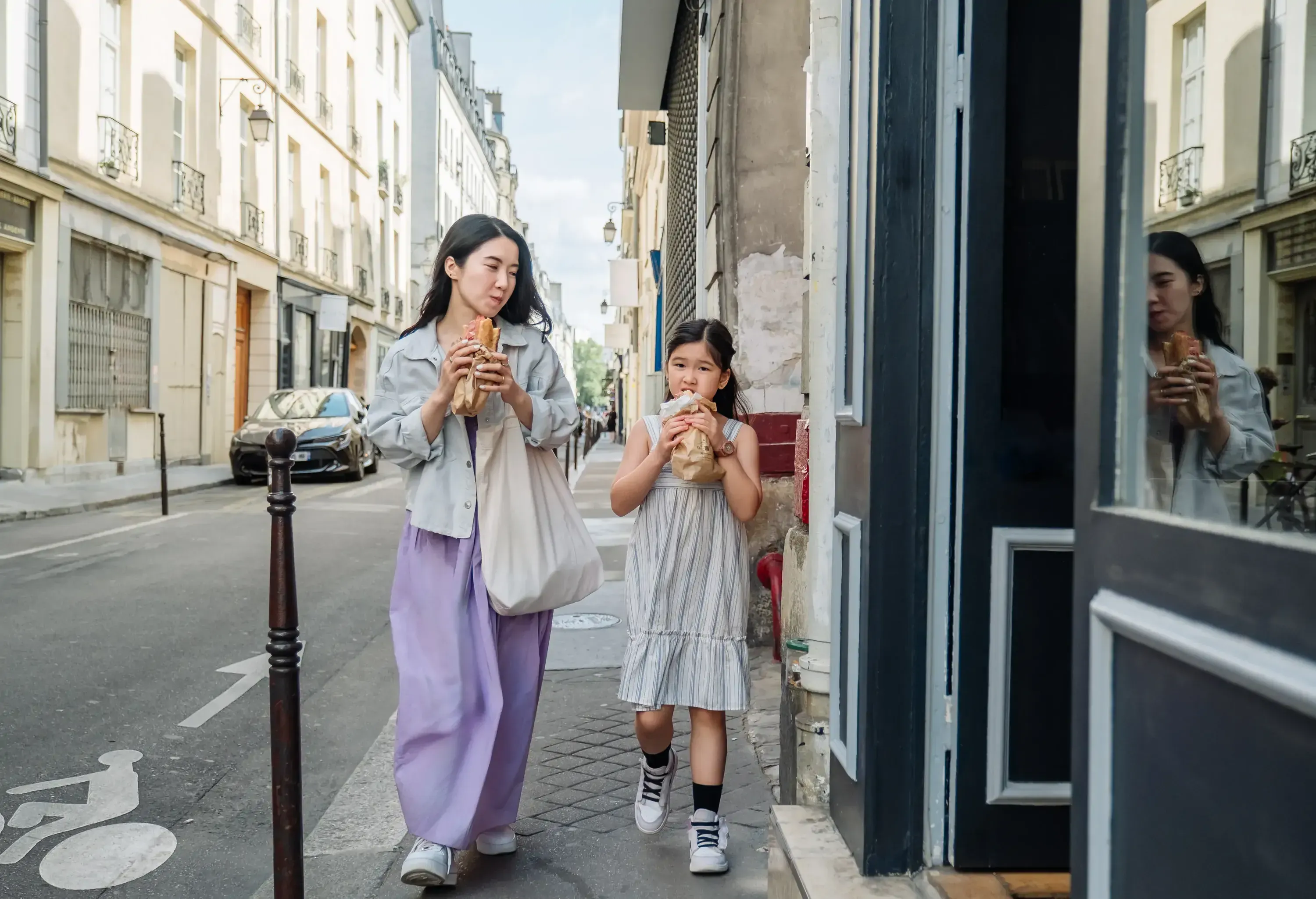 Asian woman and her little daughter enjoying local food on street while visiting Paris. Concept of family weekend activities, holiday, travel, fast food, eating out.