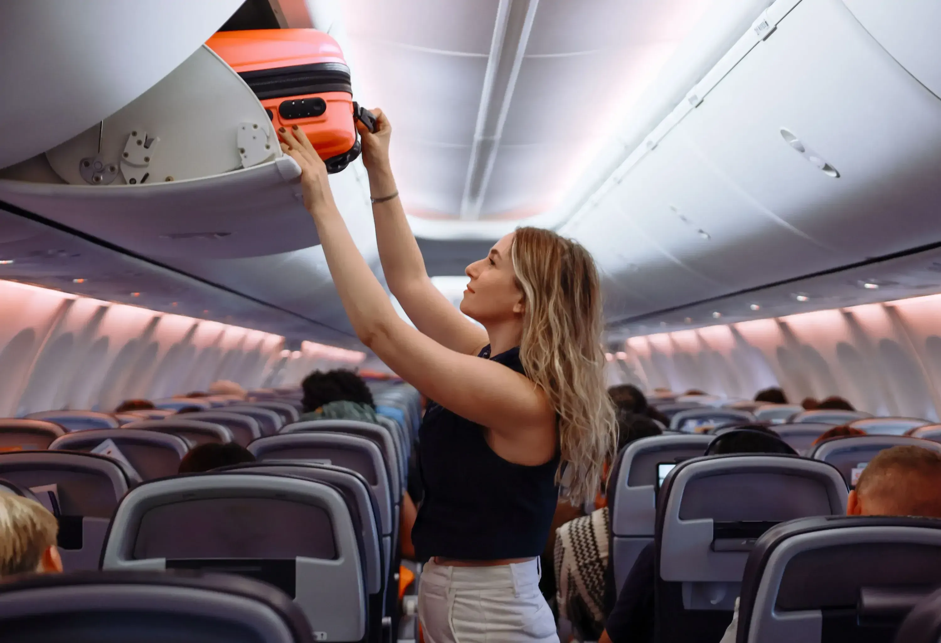 Female passenger putting hand baggage in lockers above seats of plane. hands are seen placing or retrieving a pink hard-shell suitcase from an airplane's overhead storage compartment.