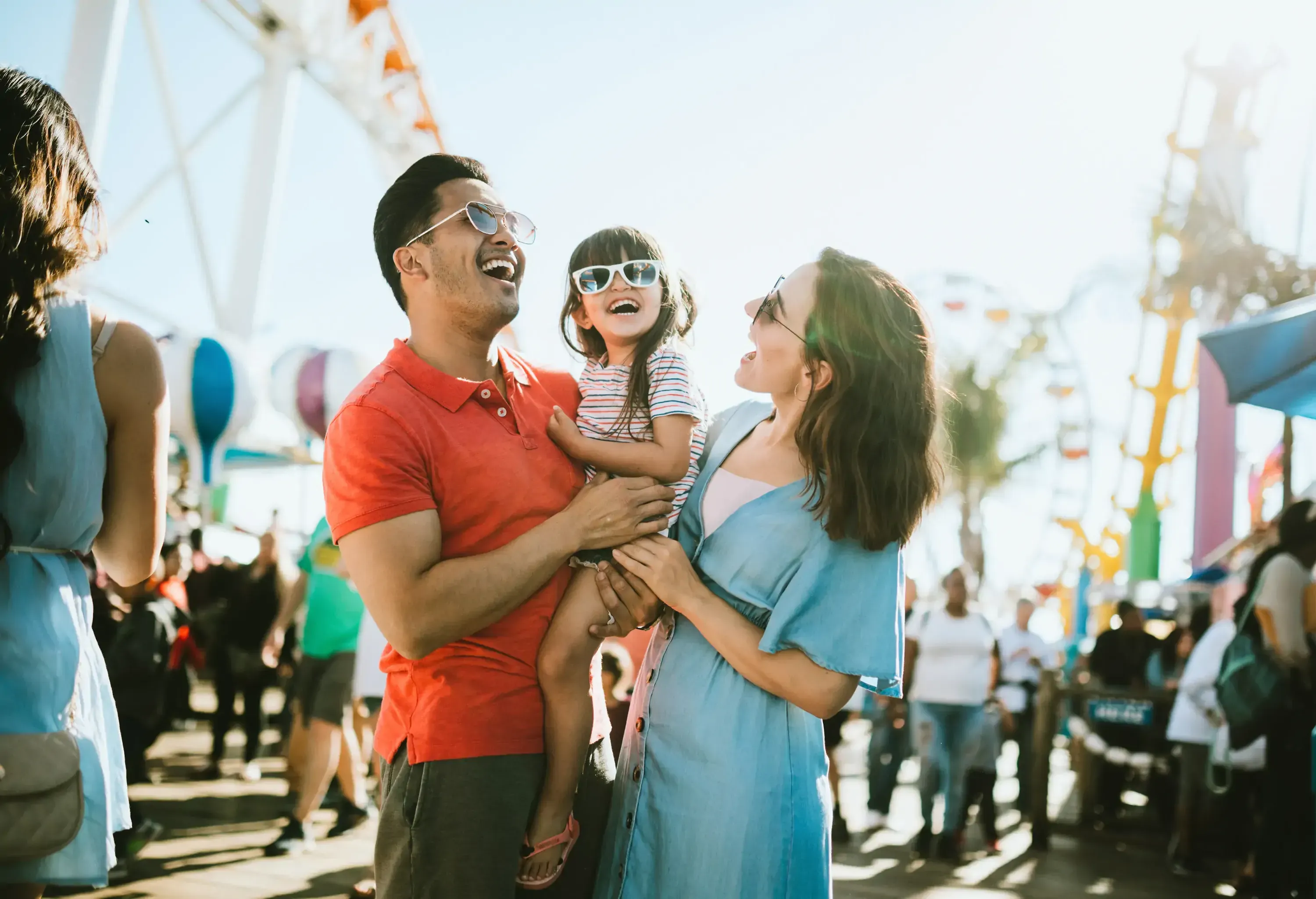 A mixed race family enjoys the rides and sun at the fair activities on Santa Monica Pier in Los Angeles, California. They all wear sunglasses with big smiles.