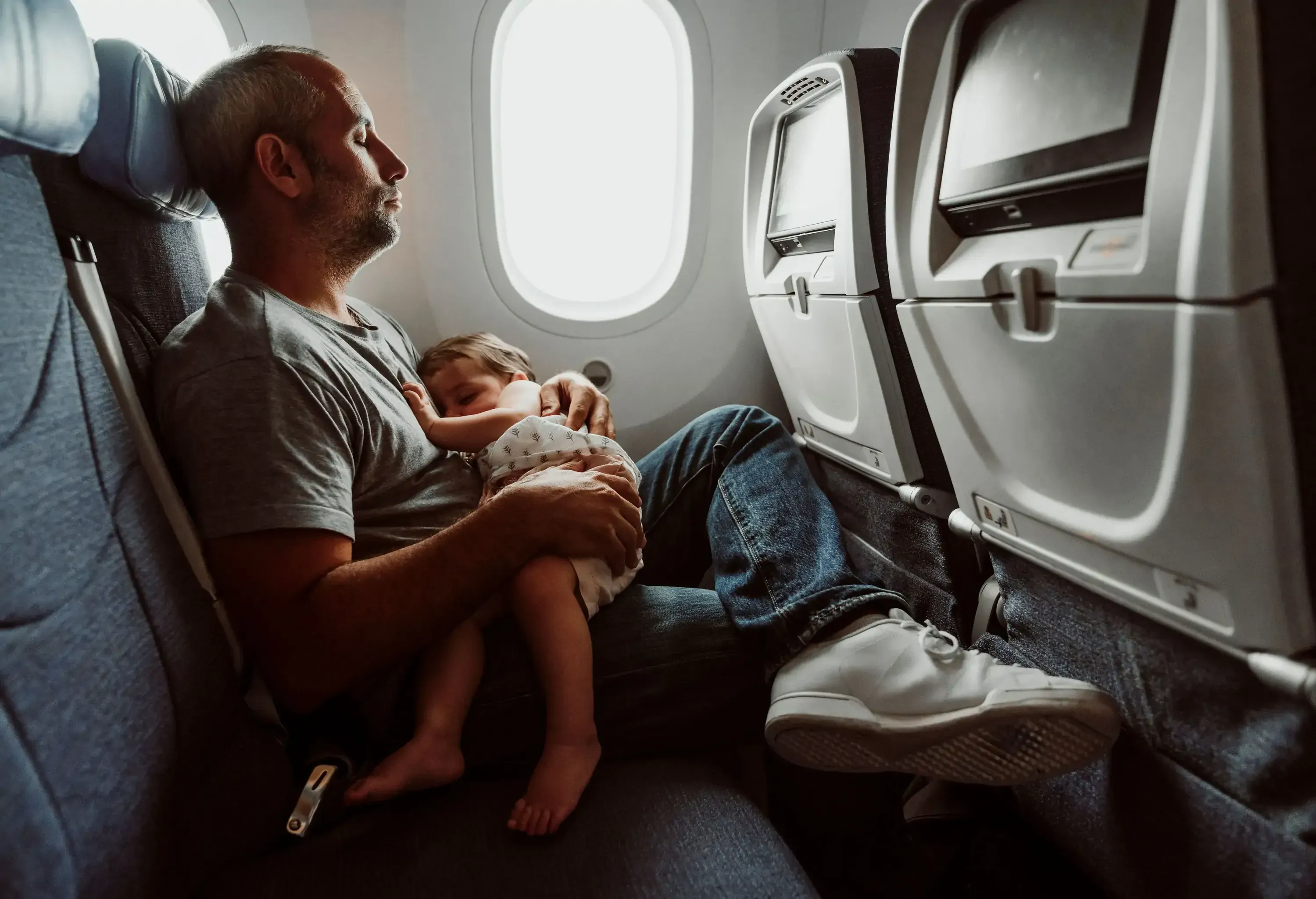 A father with baby on his lap sitting in the window seat of a plane