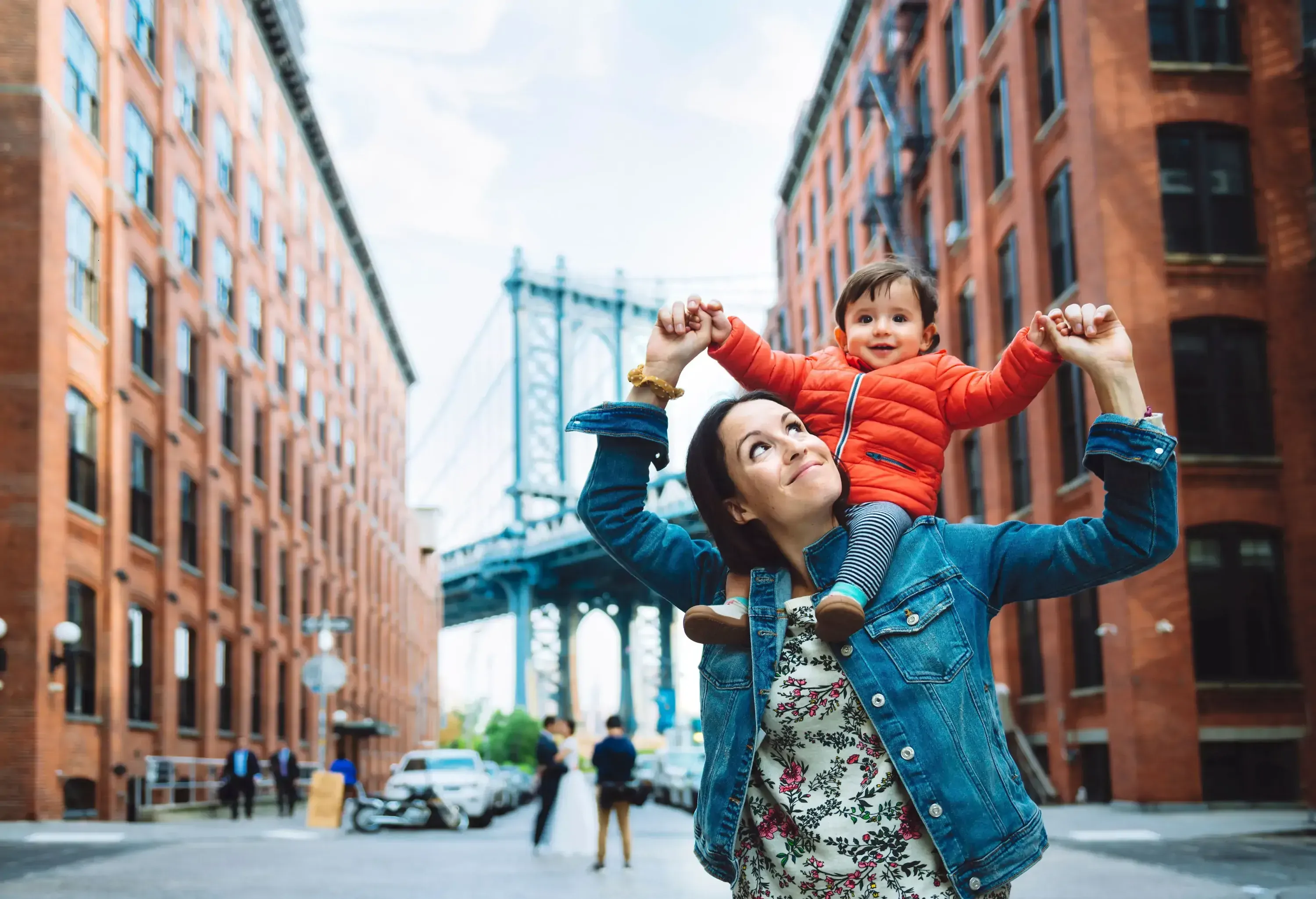 A woman carrying a small child over her shoulders standing in a New York street.