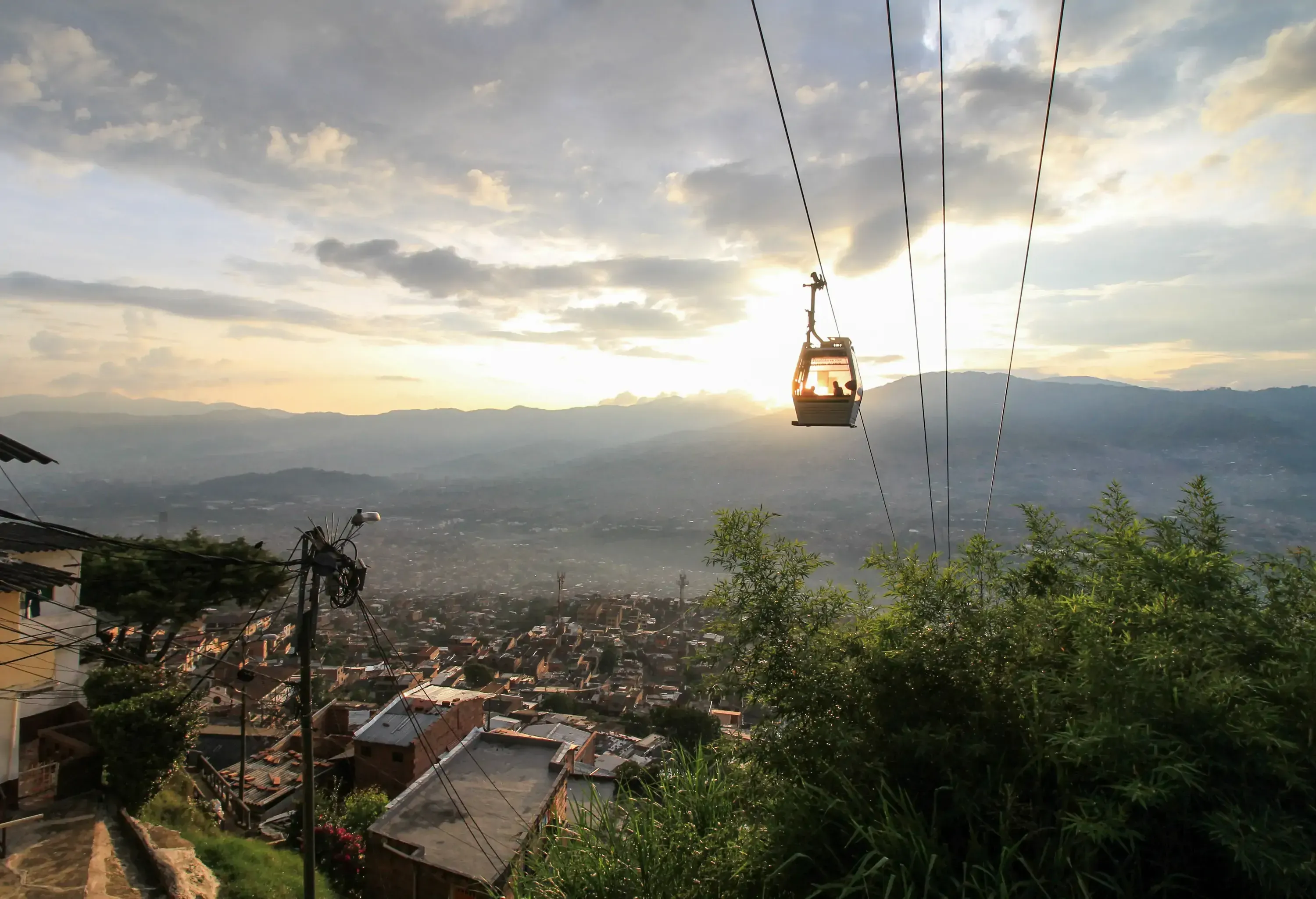 A cable car dangling over the treetops and the buildings across the valley.