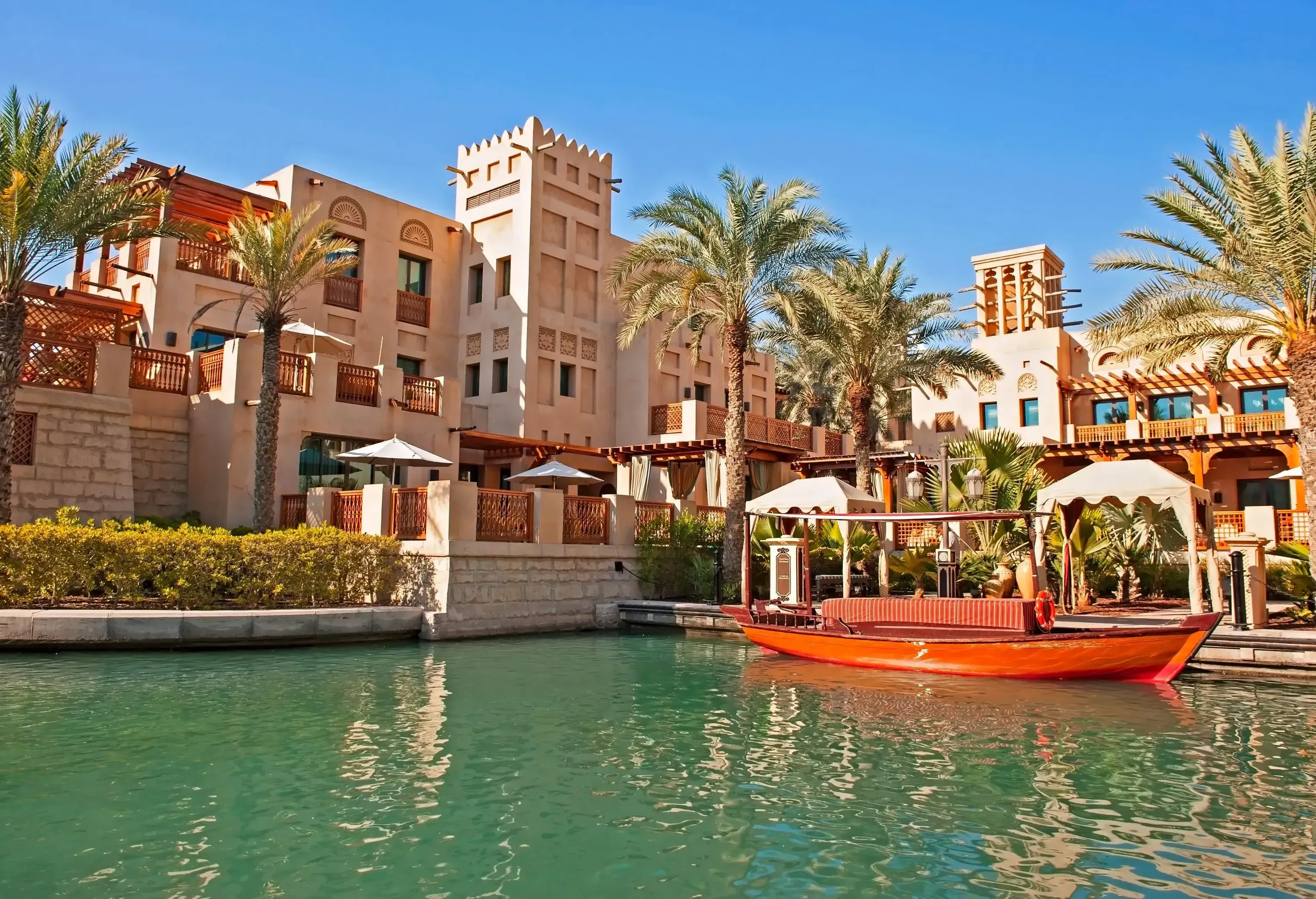 A boat at anchor in front of a boxy building with a flat roof and sharp angles on the promenade.