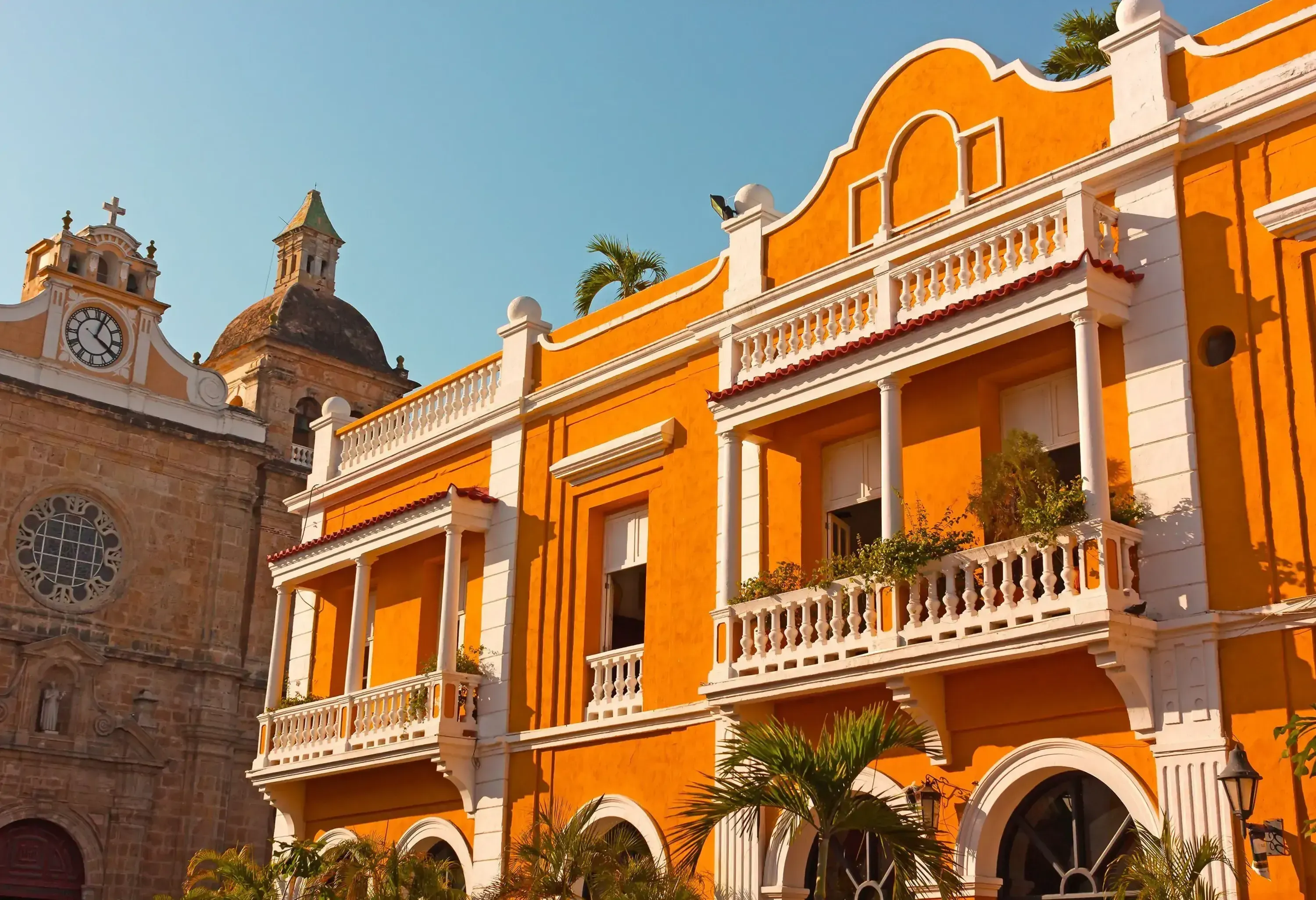 Historic colonial architecture is showcased in a building with an orange facade, lush plants adorning the balcony, and the sturdy brick structure of a church nestling in the background on the side.