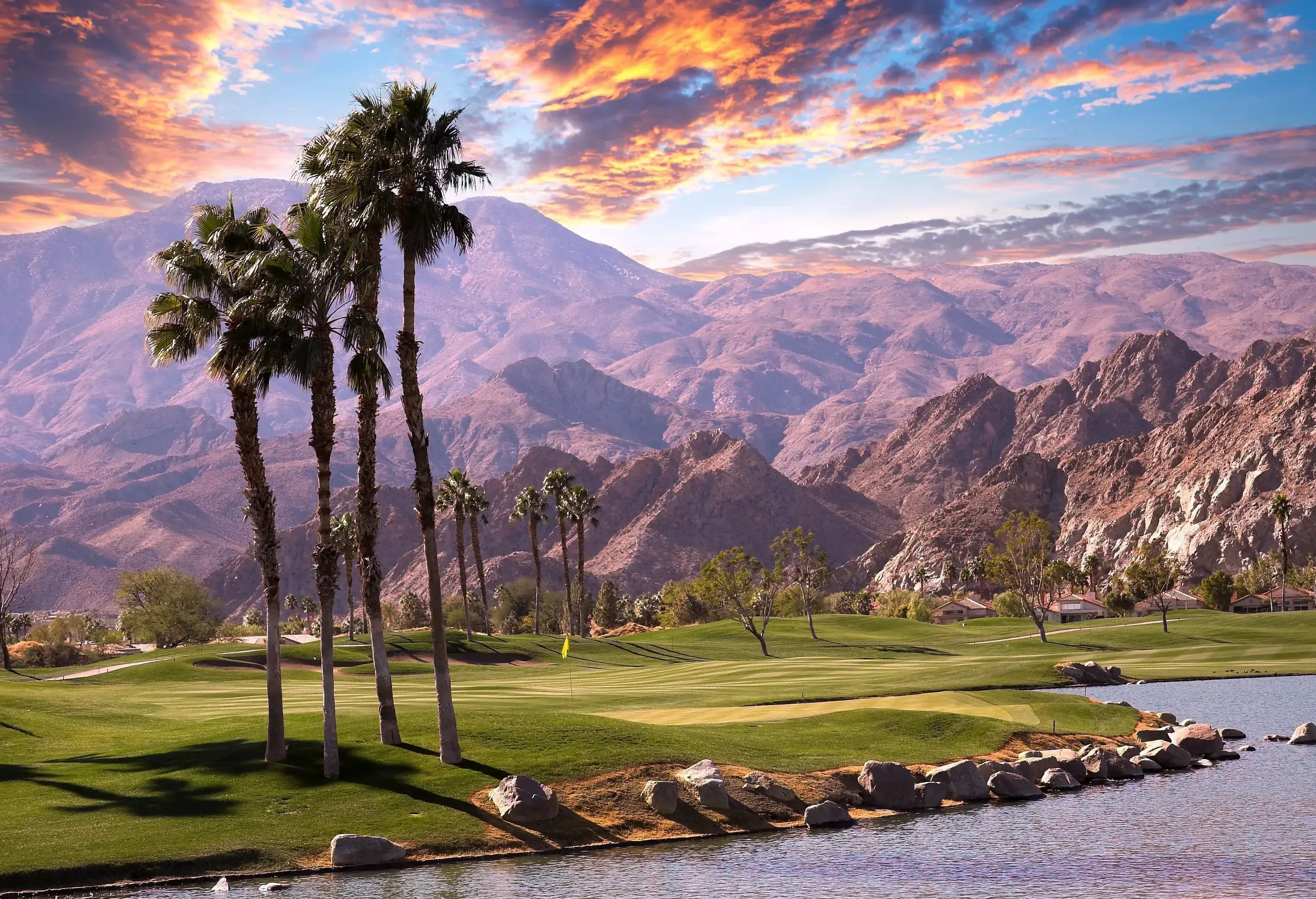 A majestic view of a lush golf course with a lagoon and the mountain range against the scenic twilight sky in the background.