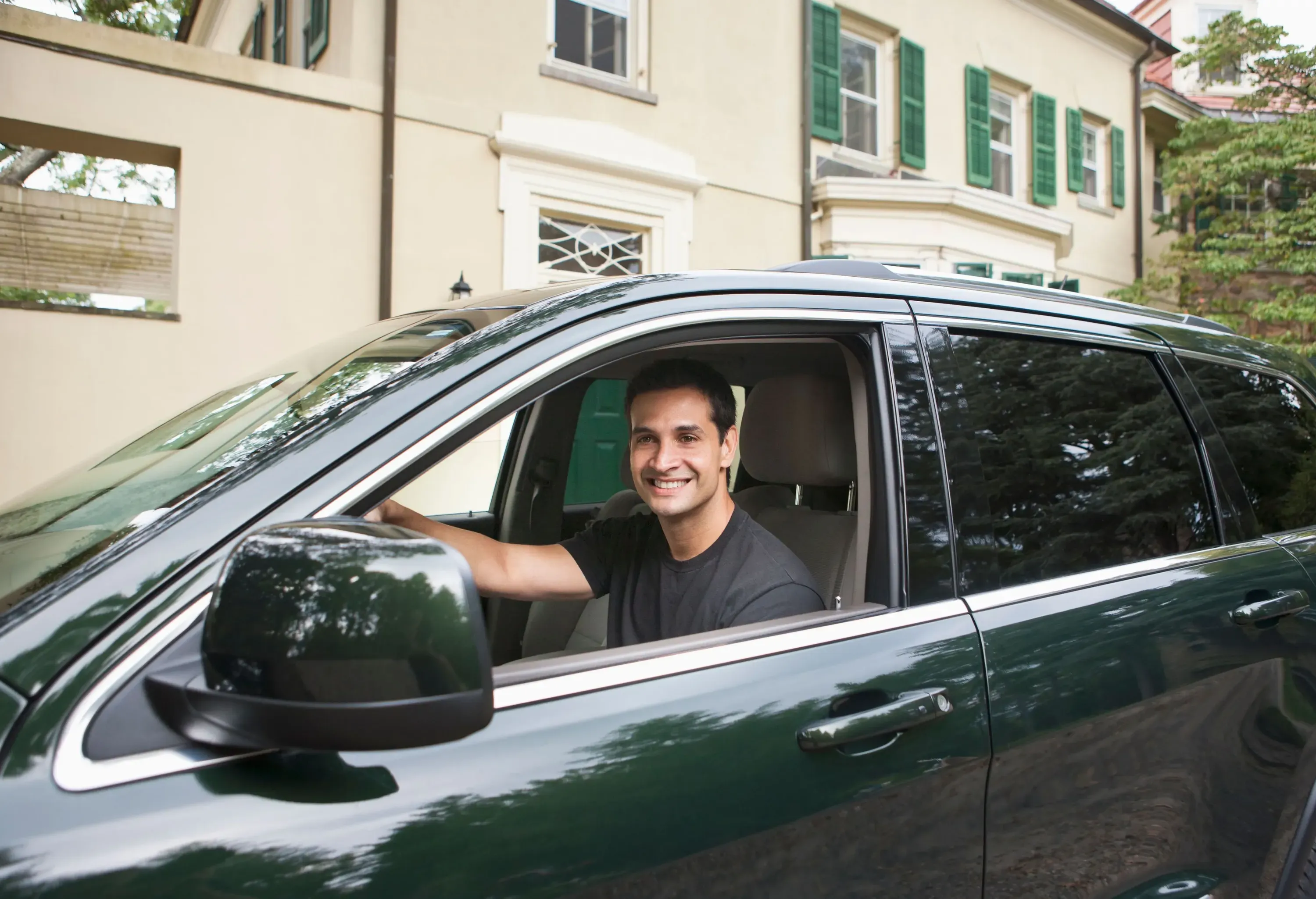 A smiling man sits in the driver's seat of a car.