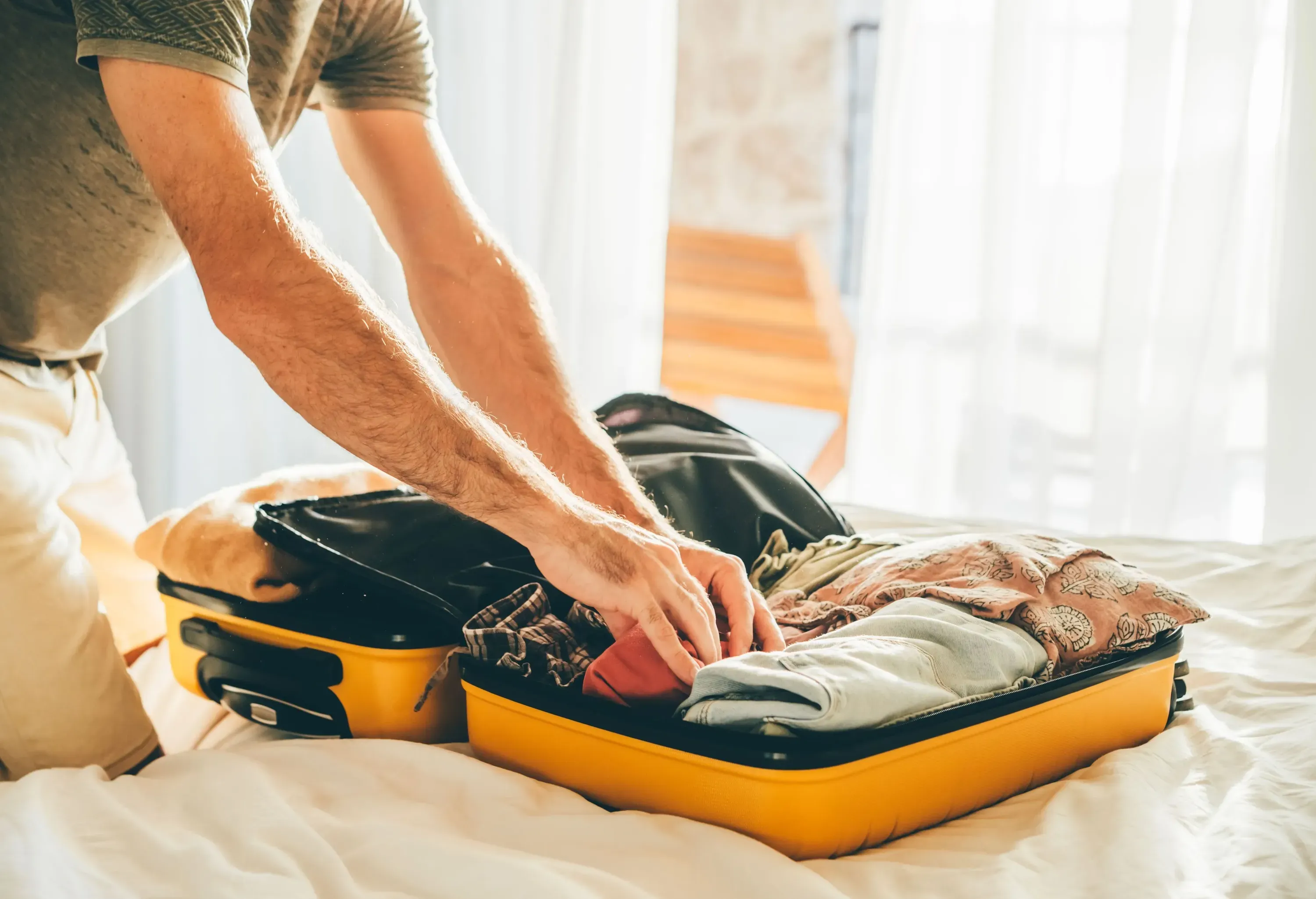 Man packing suitcase in hotel room.