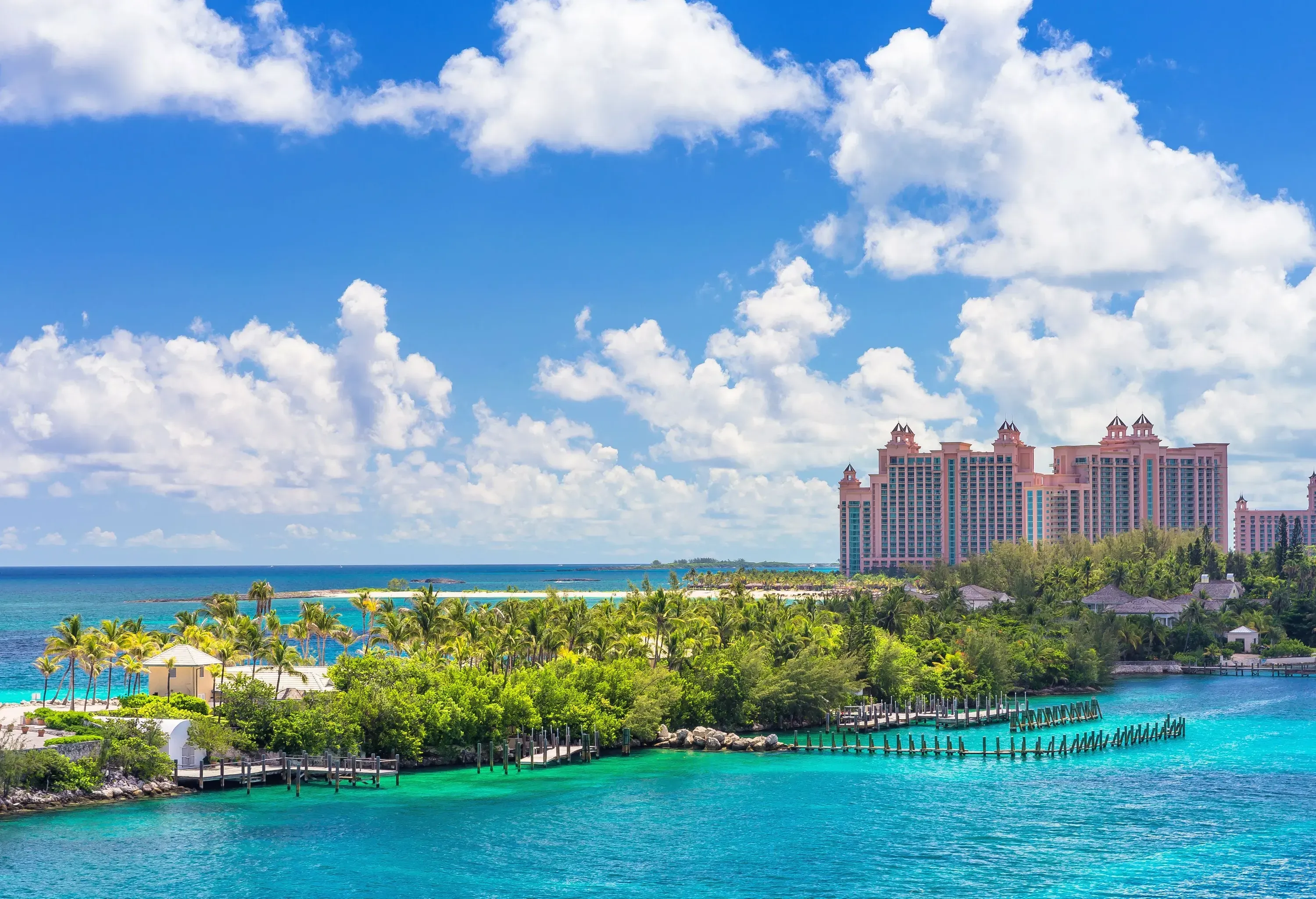 Three identical buildings stand on the coast facing the lush trees surrounded by turquoise waters under the fluffy white clouds.